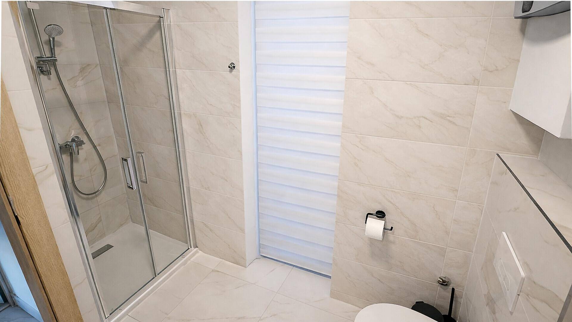 Modernes Badezimmer mit hellen Fliesen, Duschkabine und wandhängendem WC.