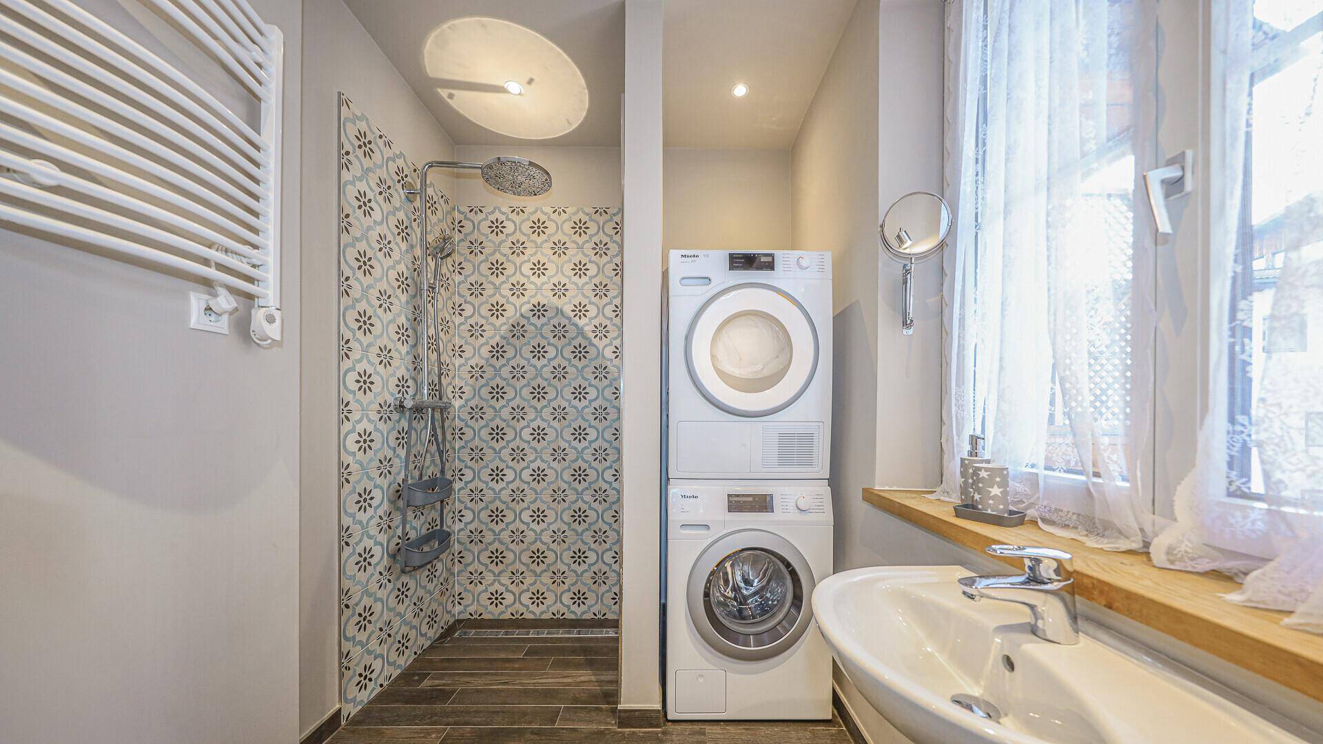 Badezimmer mit Dusche, Waschmaschine, Trockner und Fenster im funktionalen Design.