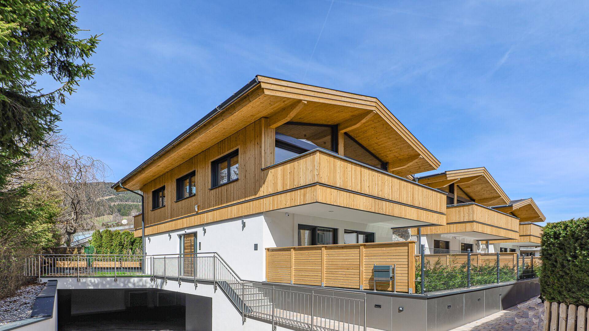 Moderne Architektur mit Holzfassade, Balkonen und Zufahrt zur Tiefgarage.