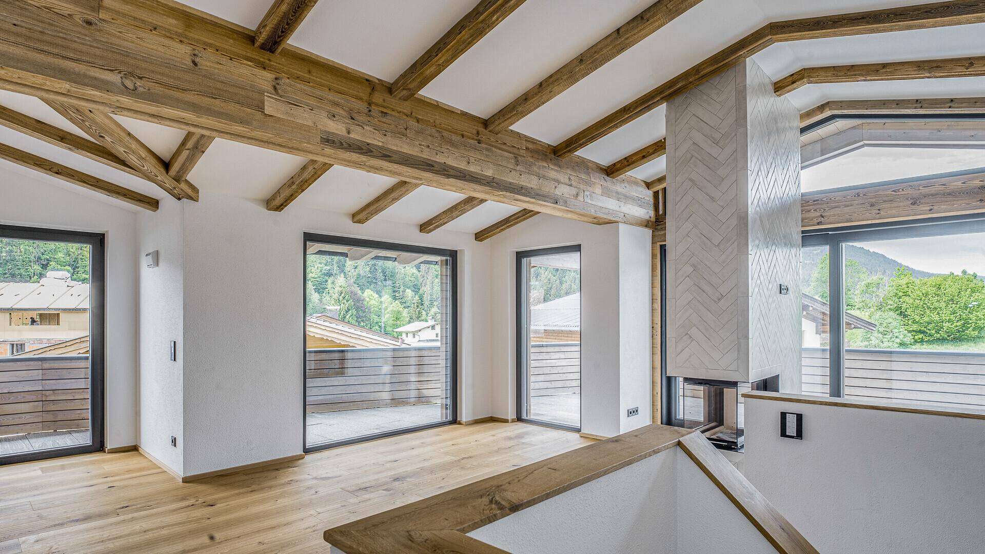 Helles Wohnzimmer mit Holzbalkendecke, Kamin und Zugang zu einem Balkon mit Bergblick.