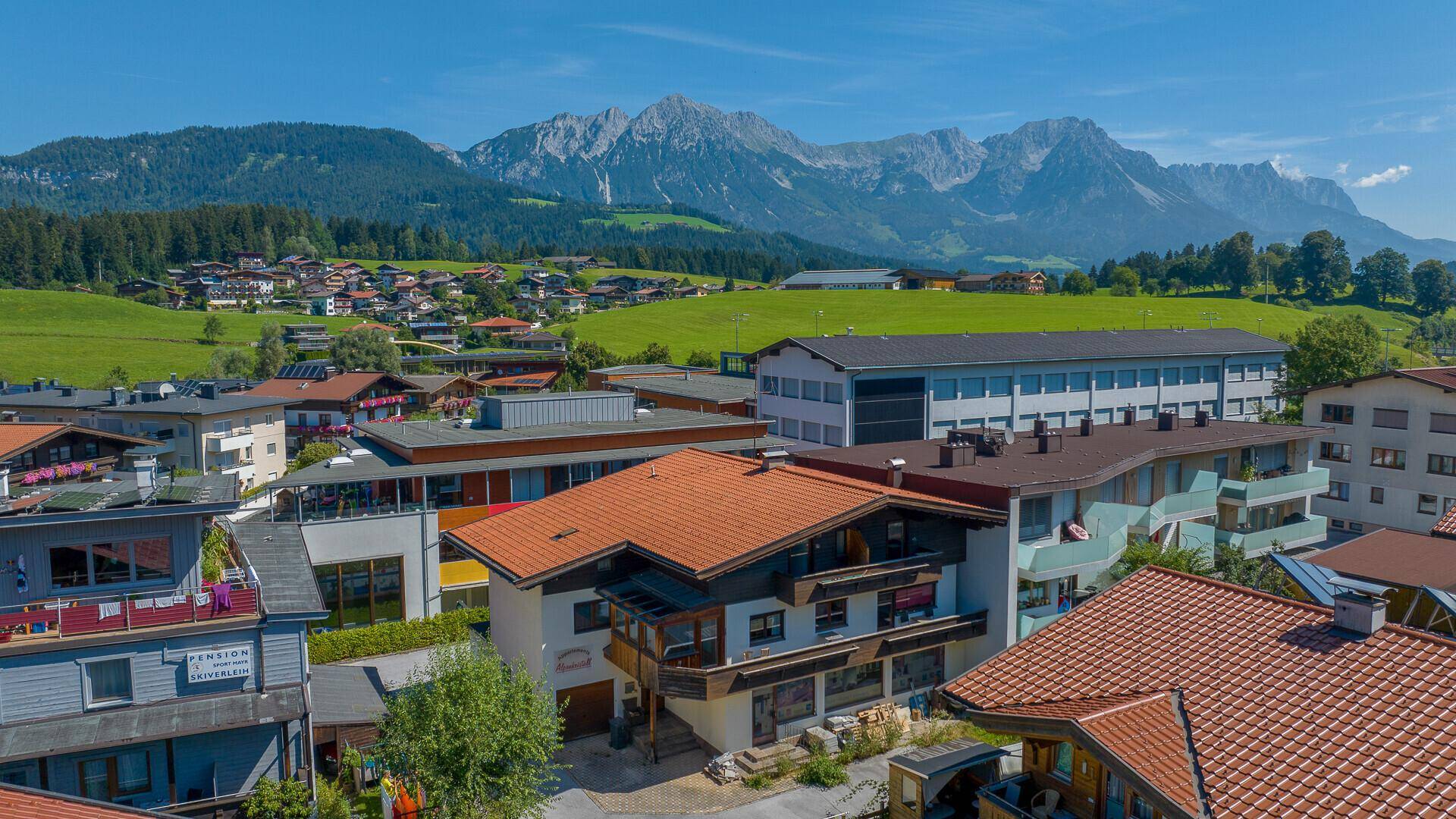 Luftaufnahme eines Dorfes in den Alpen mit traditionellen Häusern und majestätischem Bergpanorama.