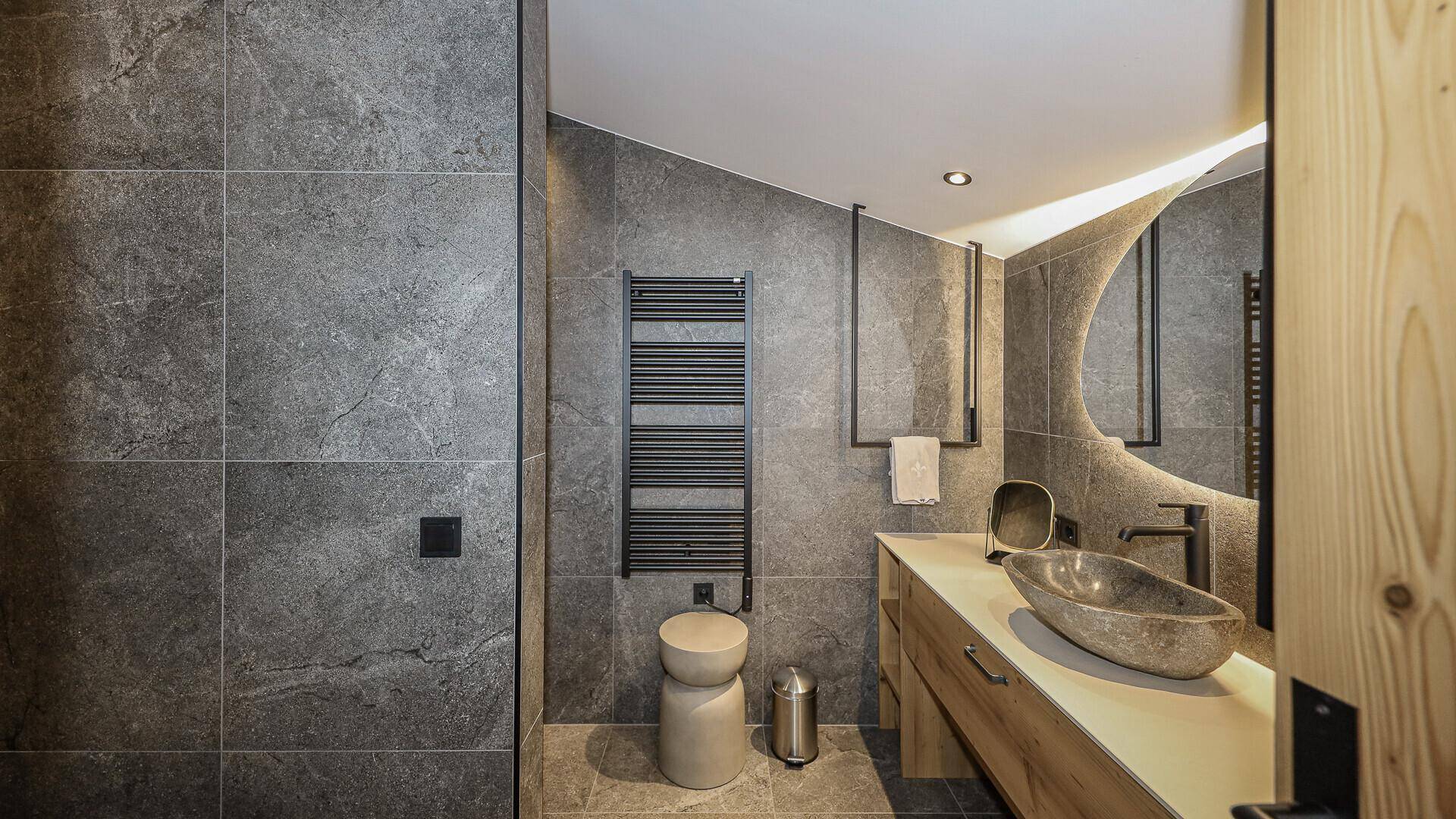 Modernes Badezimmer mit grauen Fliesen, Natursteinwaschbecken und beheiztem Handtuchhalter.