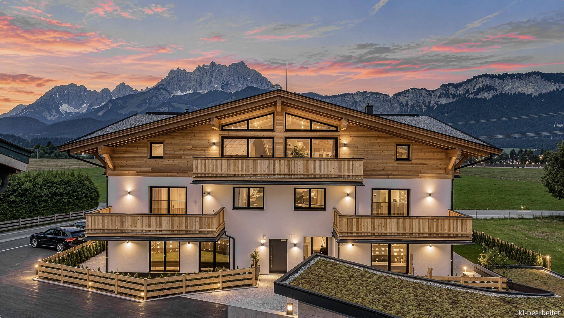 Alpines Mehrfamilienhaus mit Holzfassade, Balkonen und Bergblick in der Abenddämmerung mit Beleuchtung.