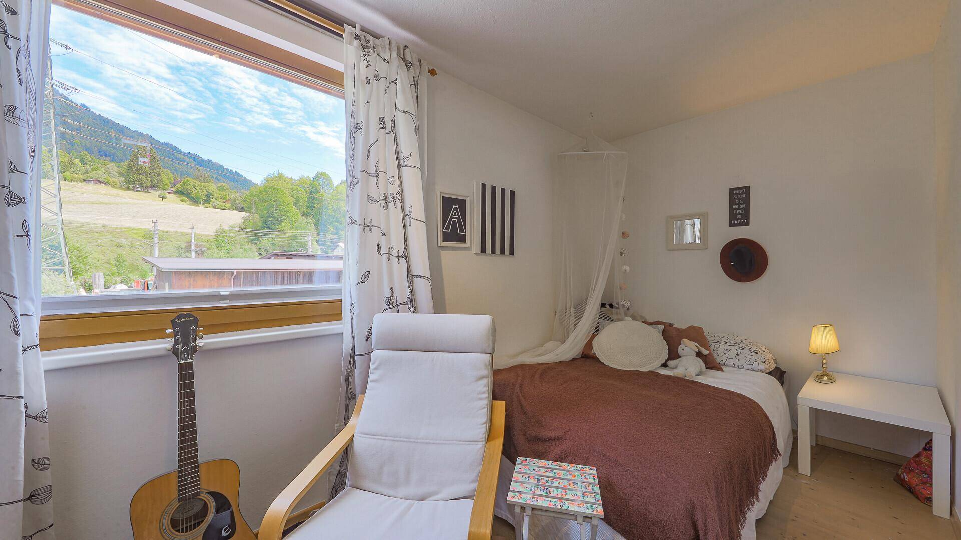 Schlafzimmer mit Bett, Gitarre und großem Fenster mit Blick auf die Berge.