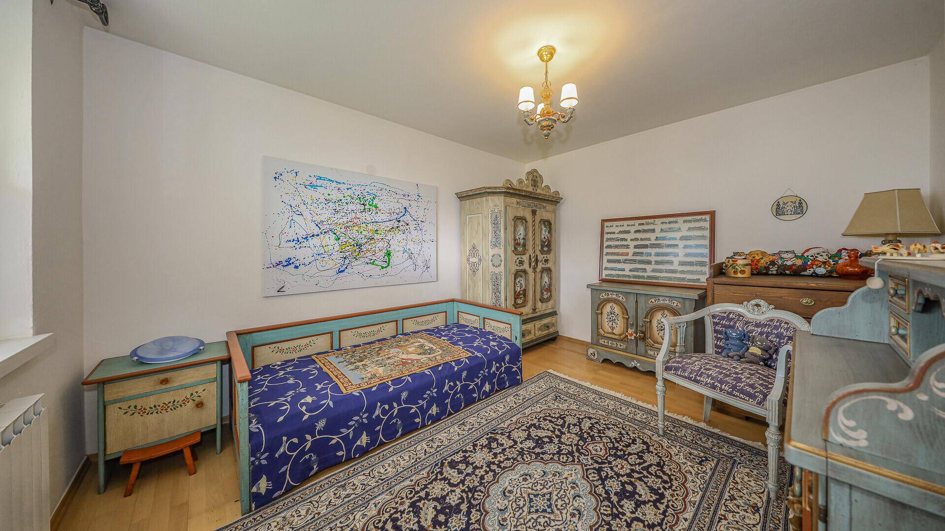 Schlafzimmer mit traditionellen, handbemalten Holzmöbeln, einem Einzelbett und einem gemusterten Teppich.
