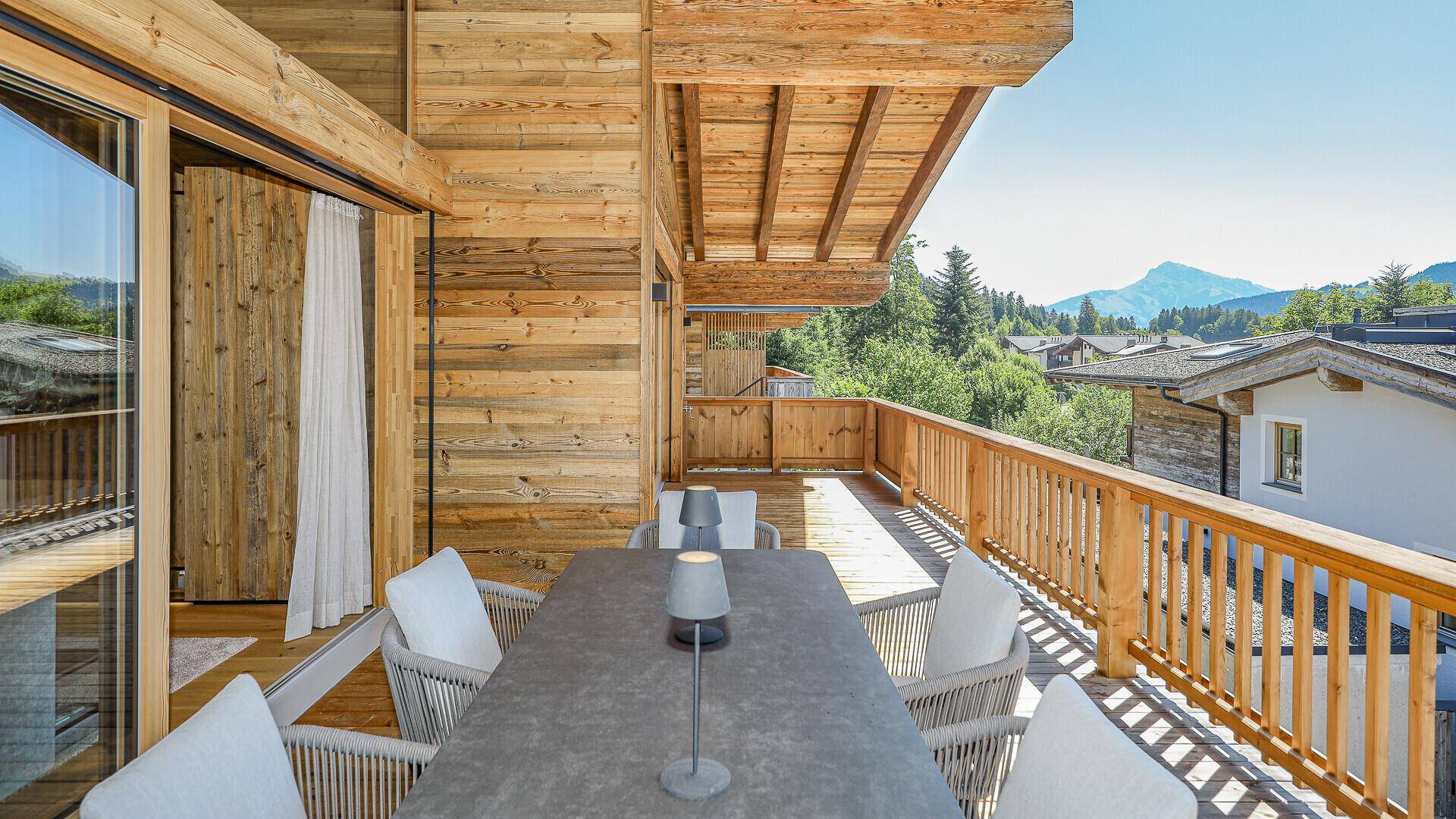 Breiter Holzbalkon mit Sitzgelegenheiten und Panoramablick auf die umliegende Berglandschaft.