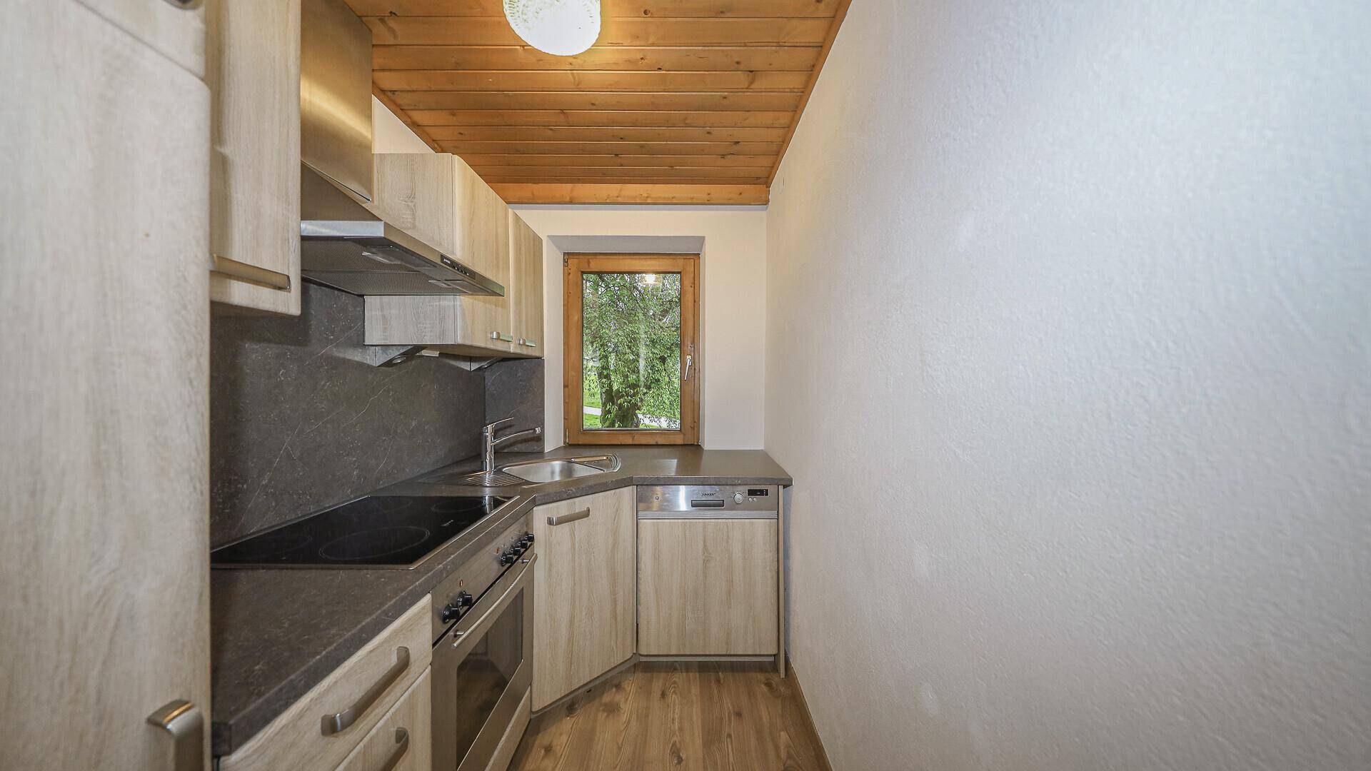 Kompakte Küche mit Holzschränken, dunkler Arbeitsplatte und Fensterblick.