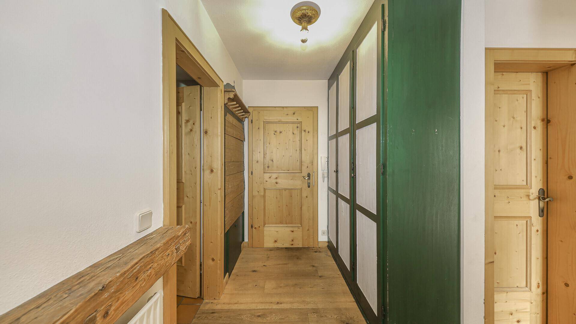 Flur mit Holzboden, Holztüren und einem grünen Einbauschrank im Landhausstil.