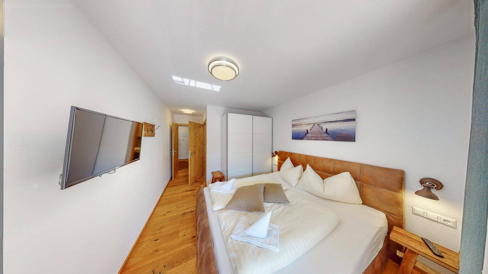 Gemütliches Schlafzimmer mit Holzbett, Parkettboden und Wandfernseher.
