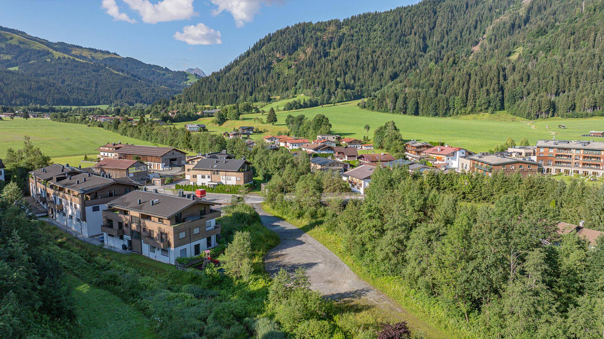 Luftaufnahme der Wohnsiedlung mit modernen Gebäuden, umgeben von Natur und Bergen.