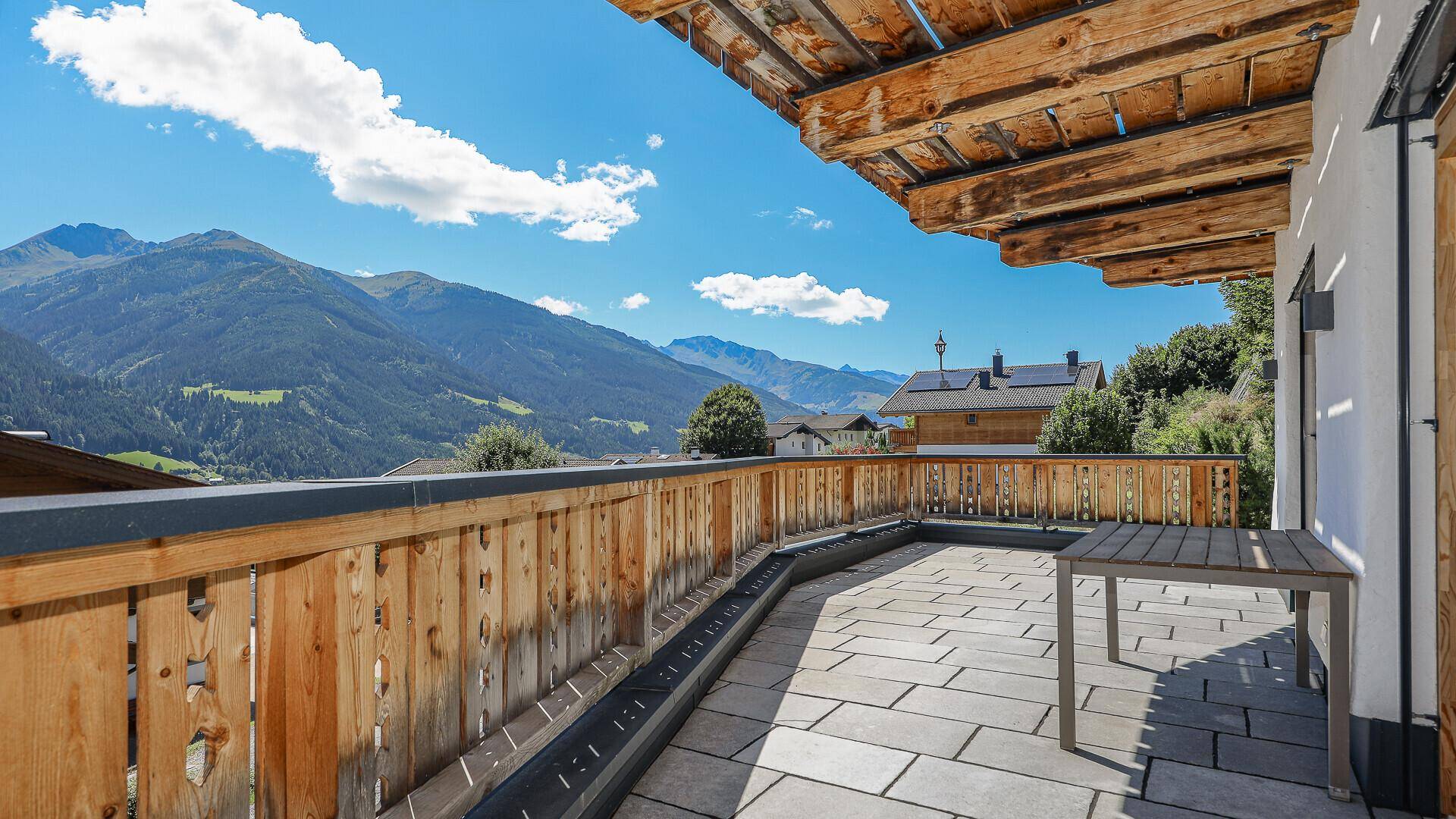 Weitläufige Terrasse mit Steinplatten, Holzgeländer und Panoramablick auf die Berge.