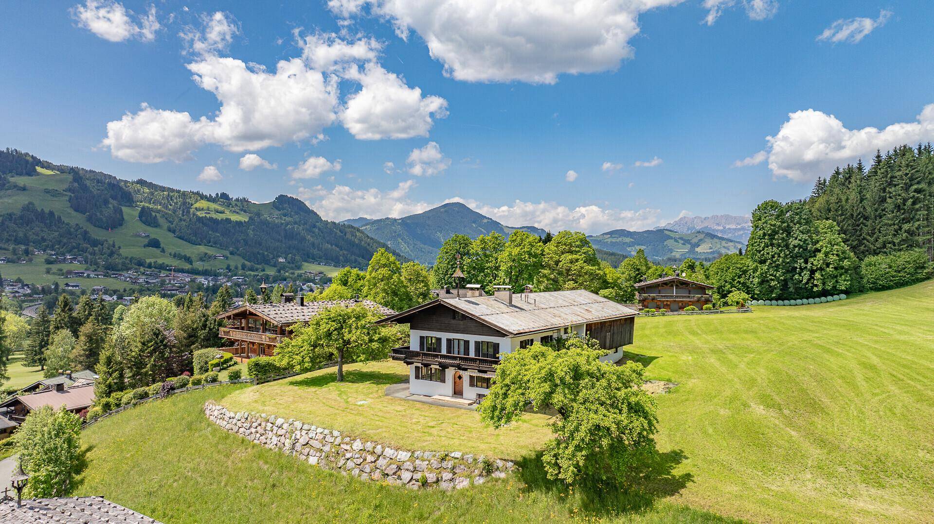 Traditionelles Haus in idyllischer Berglandschaft mit weiten grünen Wiesen und blauem Himmel.