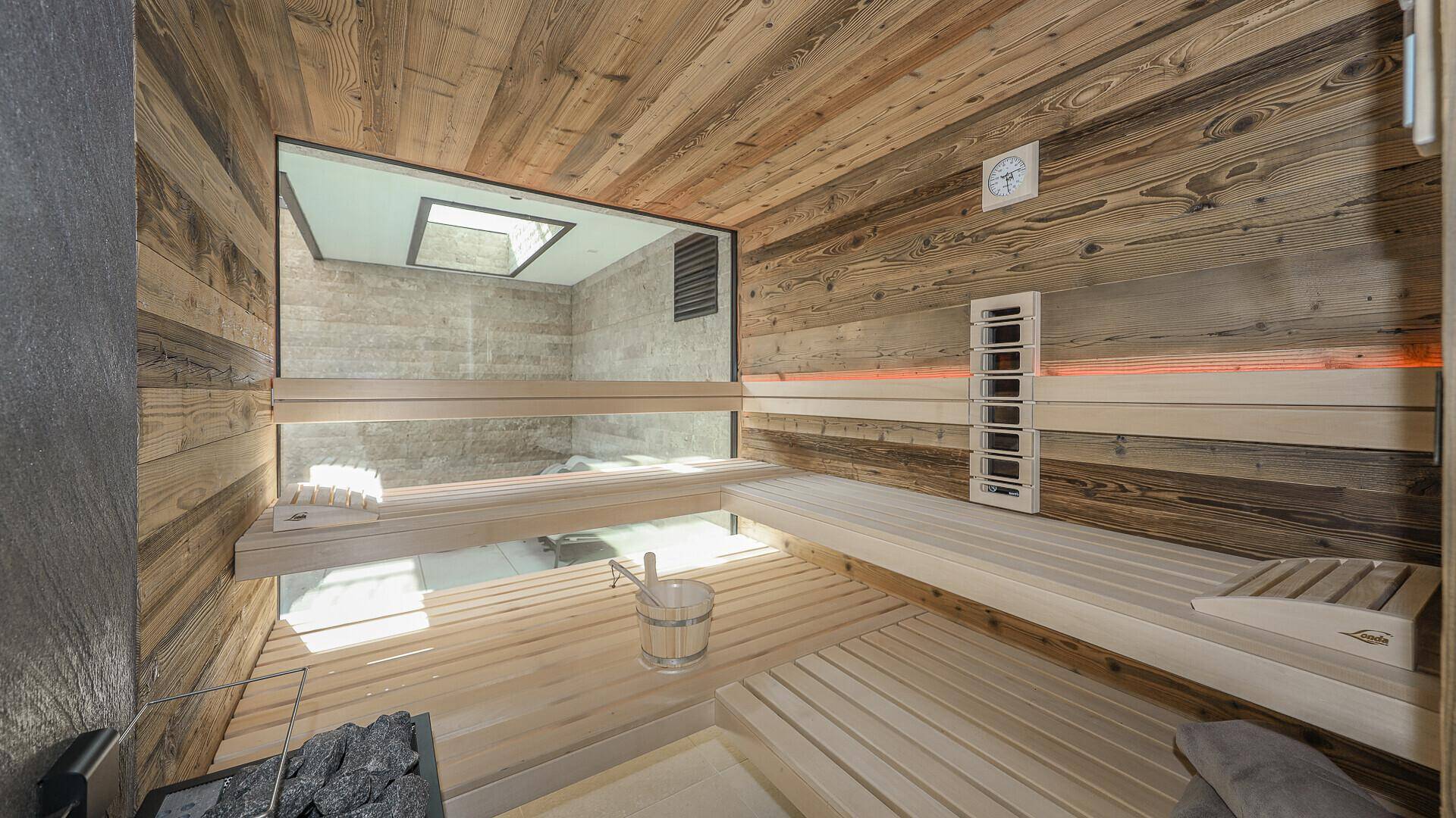 Moderne Sauna mit Holzverkleidung, bequemen Bänken und Blick in einen angrenzenden Entspannungsbereich.