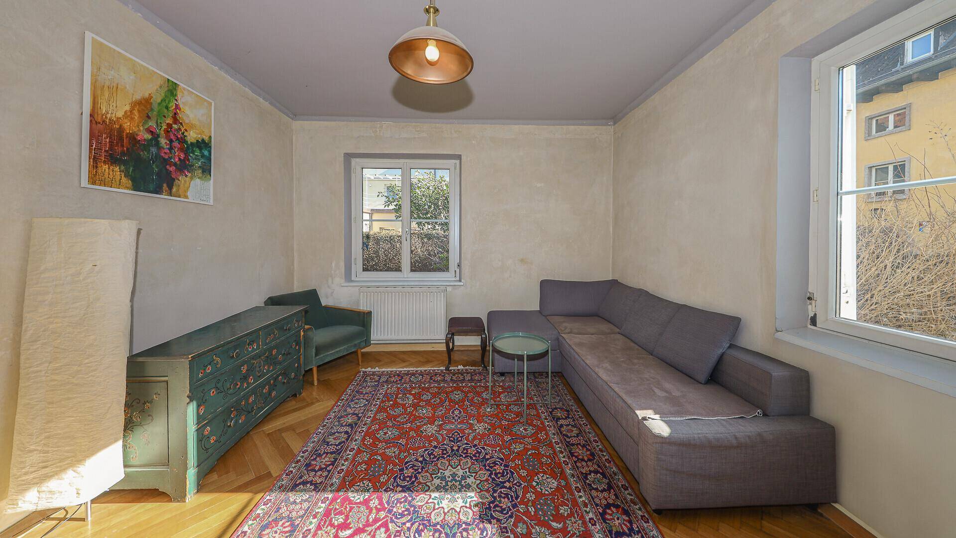 Helles Wohnzimmer mit Ecksofa, Holzboden und Blick auf die Umgebung.