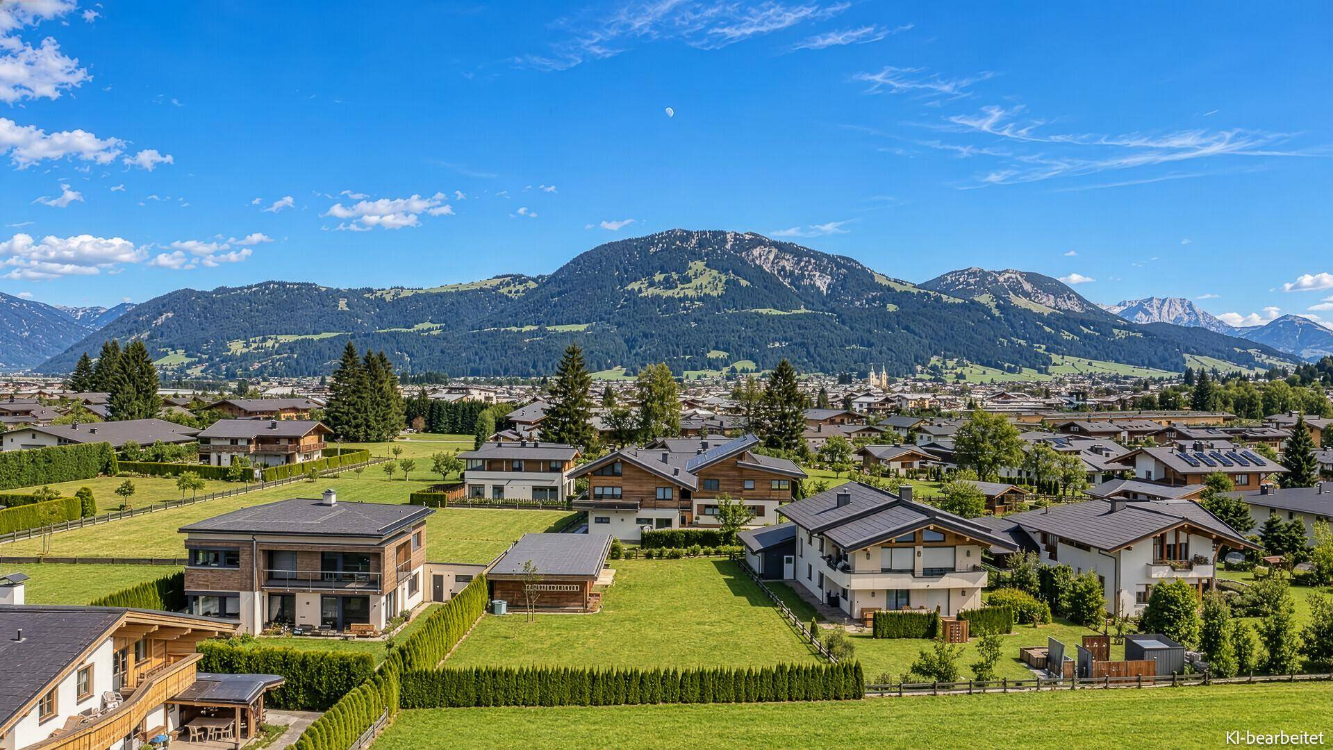 Weitläufige Wohnsiedlung mit vielen Häusern und grünen Wiesen vor einer beeindruckenden Bergkulisse.