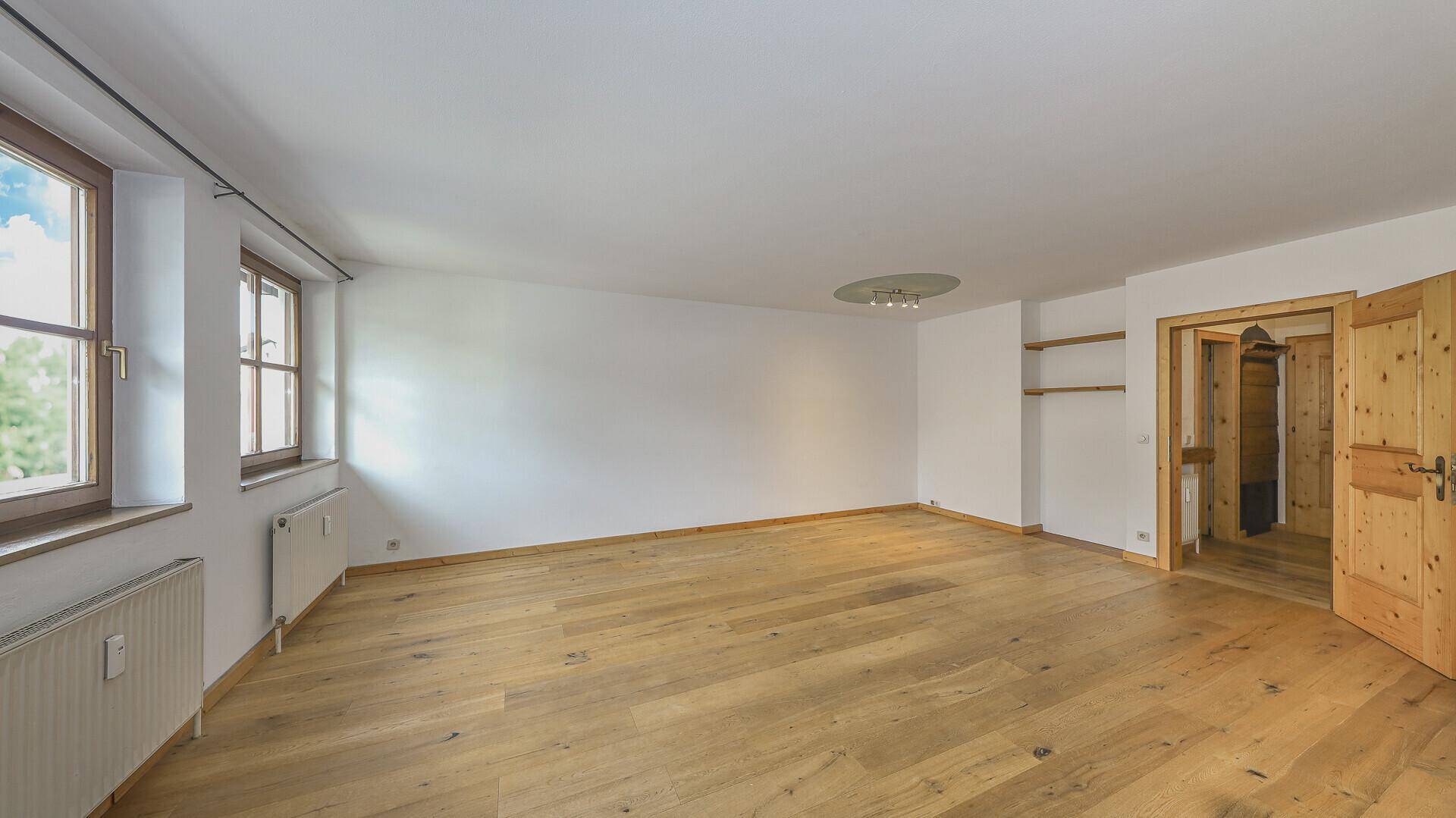 Geräumiges, leeres Wohnzimmer mit Holzboden und zwei Fenstern, bereit zur individuellen Gestaltung.