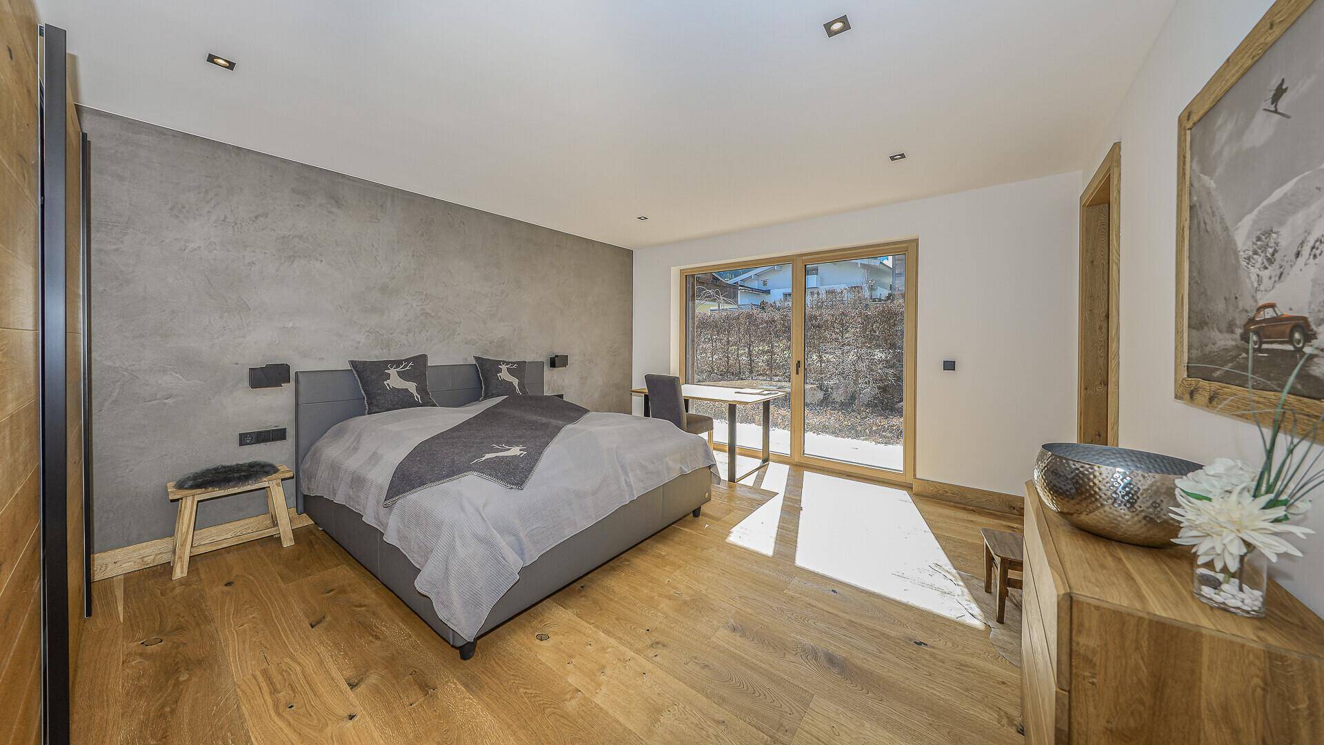 Schlafzimmer mit Holzboden, grauen Wänden und viel Tageslicht.