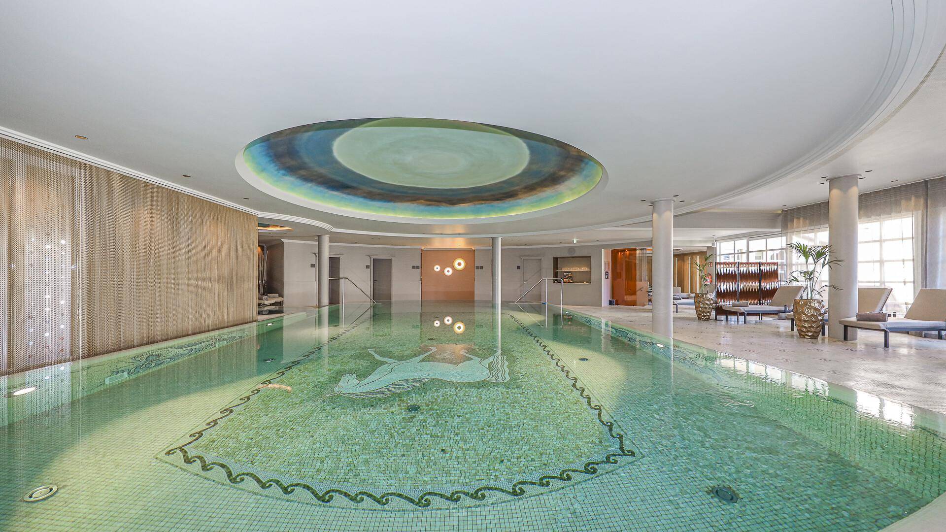 Großzügiger Innenpoolbereich mit Mosaikfliesen und dekorativer Deckenmalerei.