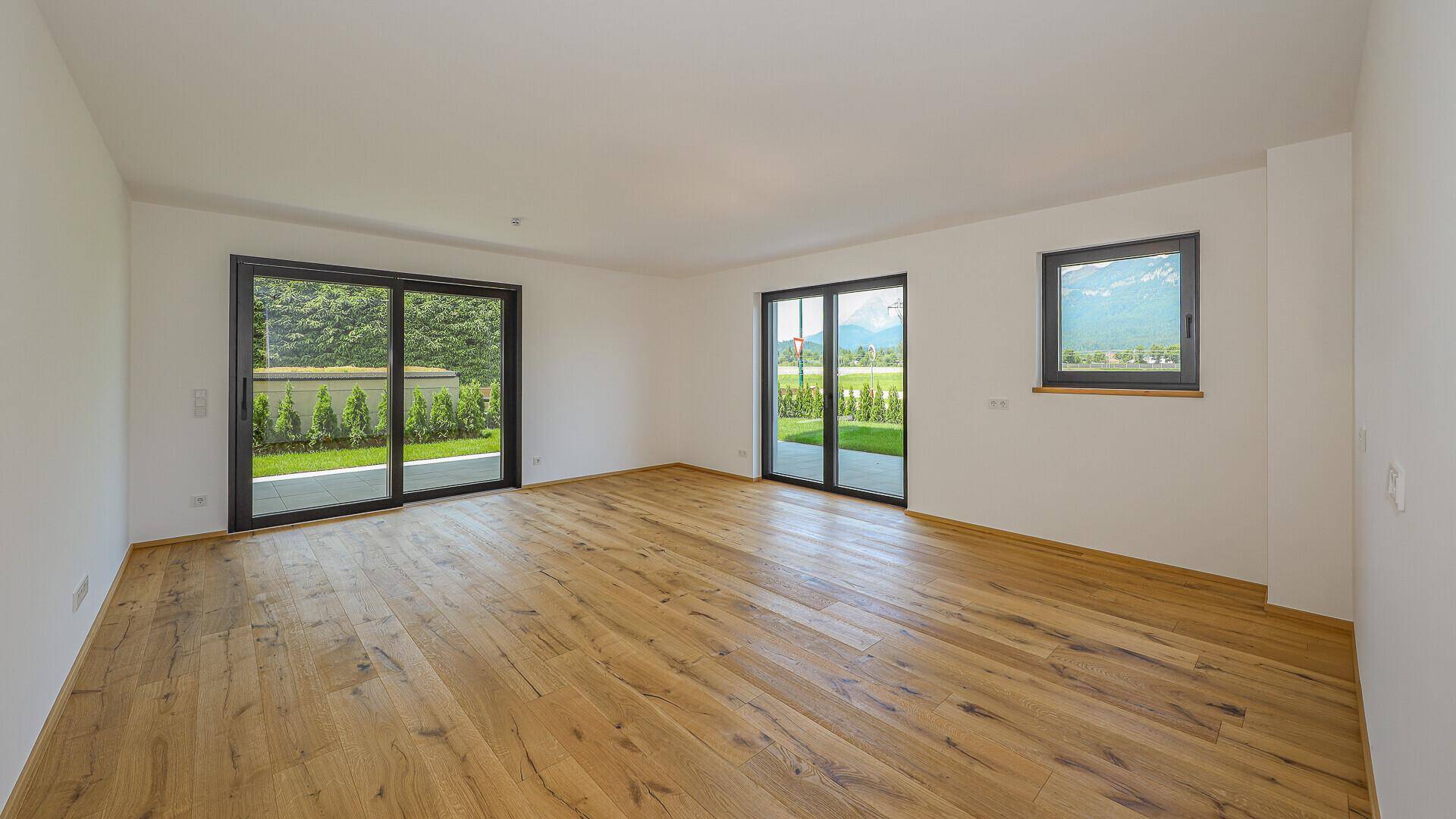 Heller, leerer Wohnraum mit Holzboden, großen Schiebetüren und Bergblick.