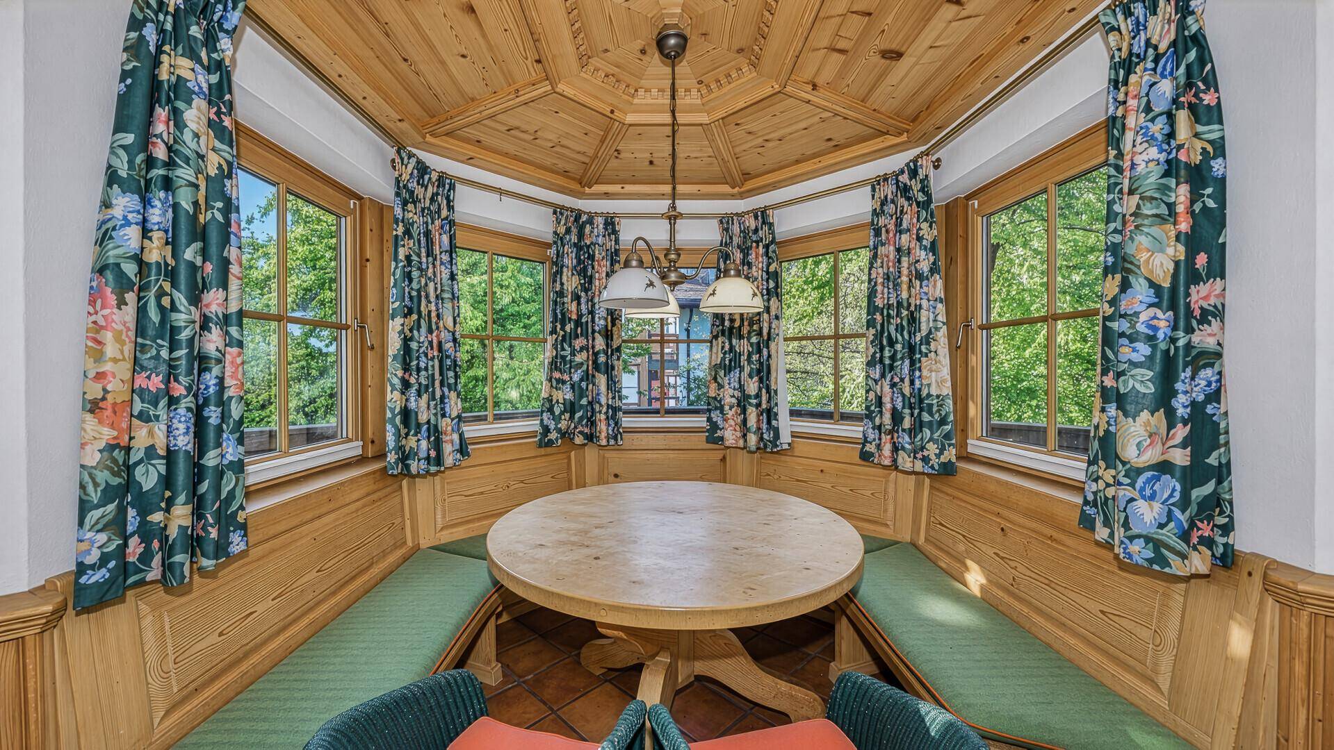 Traditionelle Essecke mit Holztisch und Bänken, umgeben von Holzvertäfelung und Fenstern mit grüner Aussicht.