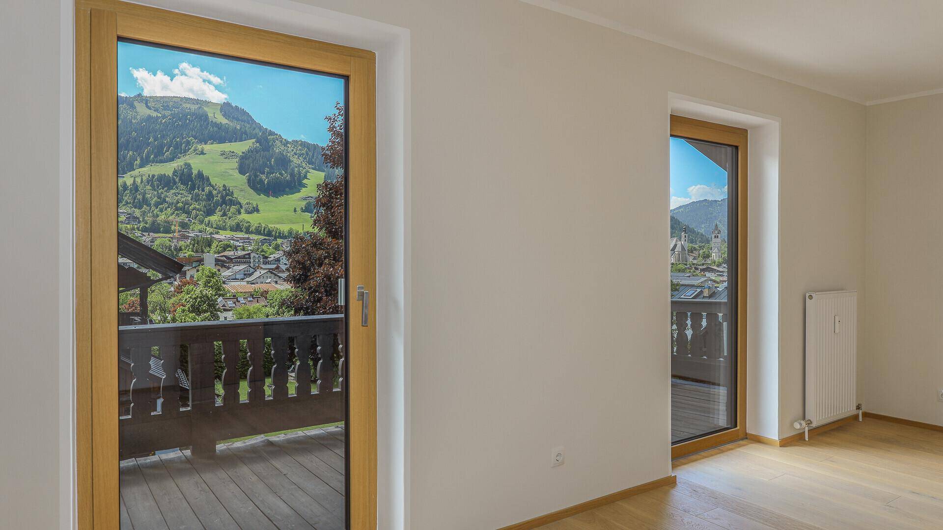 Helles Zimmer mit Holzboden und Zugang zum Balkon, bietet einen weiten Blick auf die Berge und das Tal.