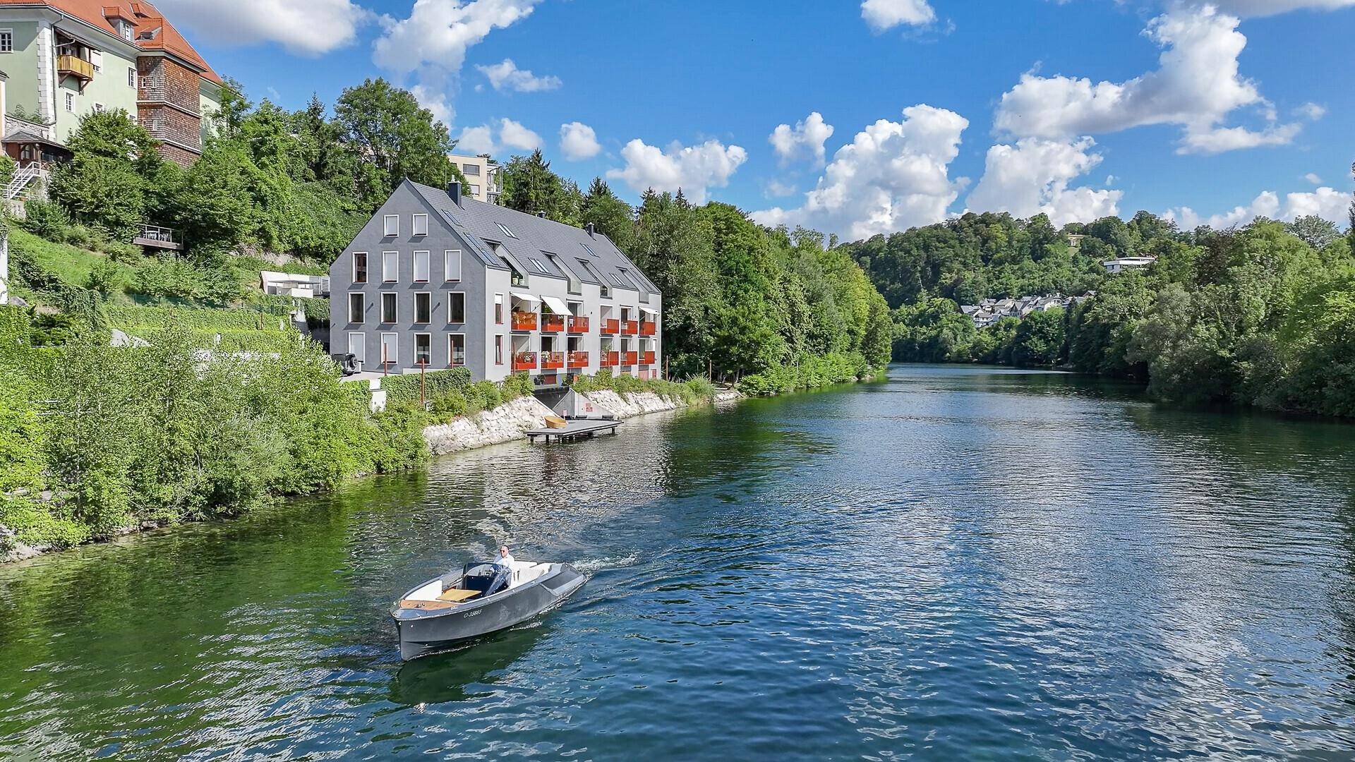 Modernes Wohngebäude am Flussufer mit Balkonen und umgeben von üppiger Natur.