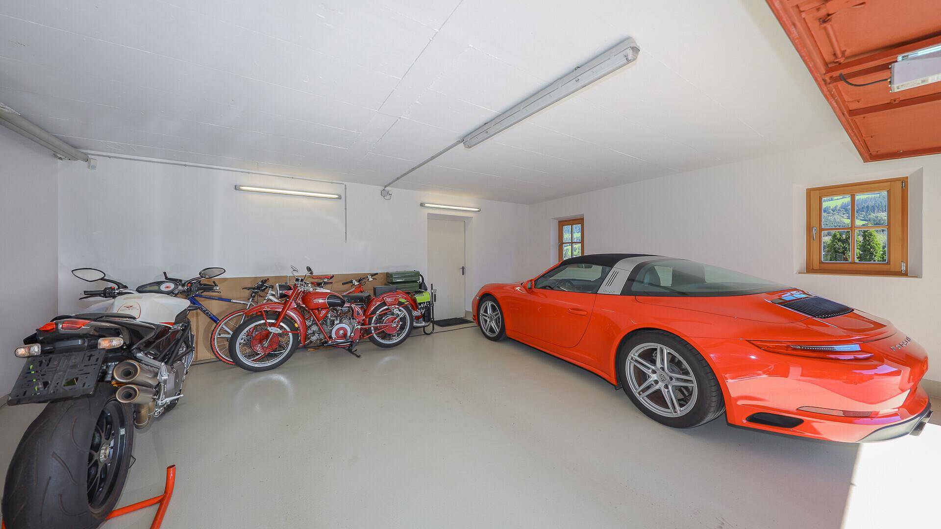 Geräumige Garage mit Platz für mehrere Fahrzeuge und Motorräder, gut beleuchtet.