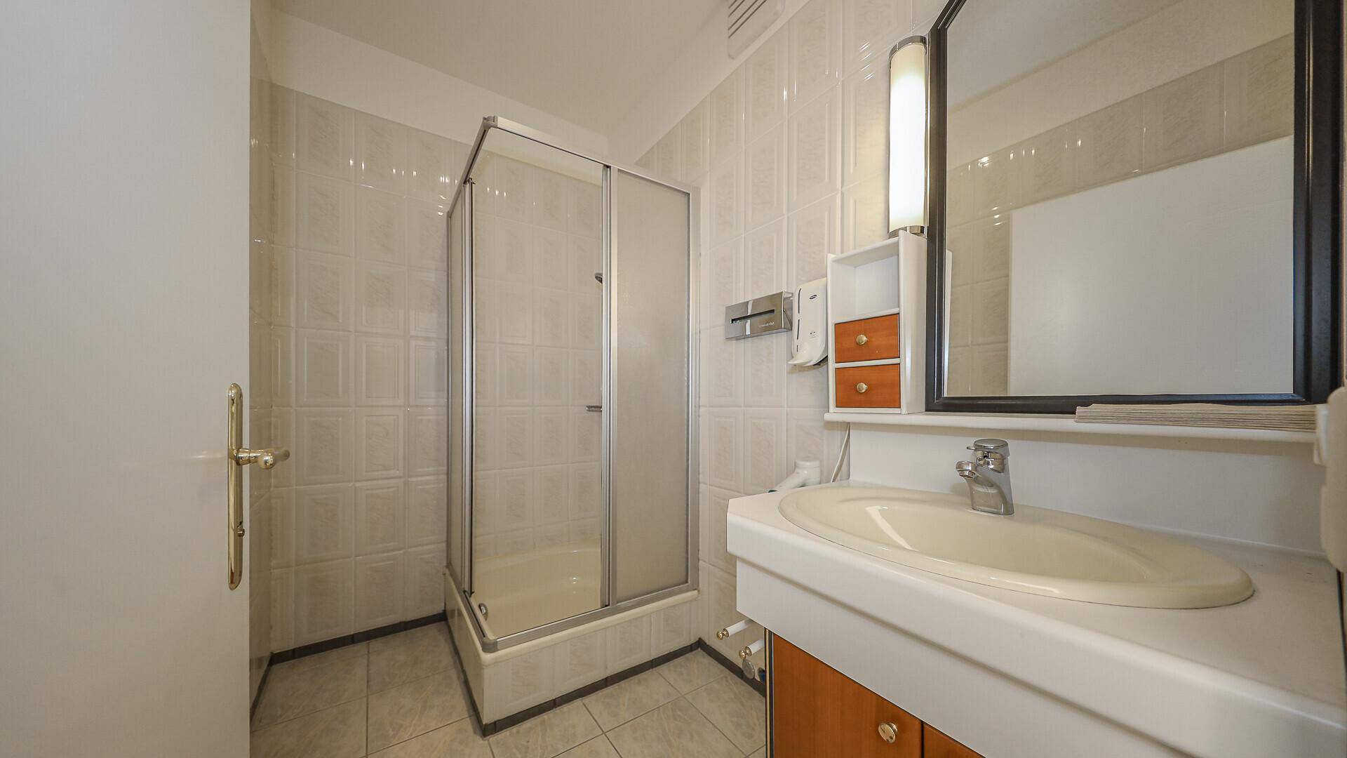 Funktionales Badezimmer mit Duschkabine, Einzelwaschbecken und hellen Fliesen.