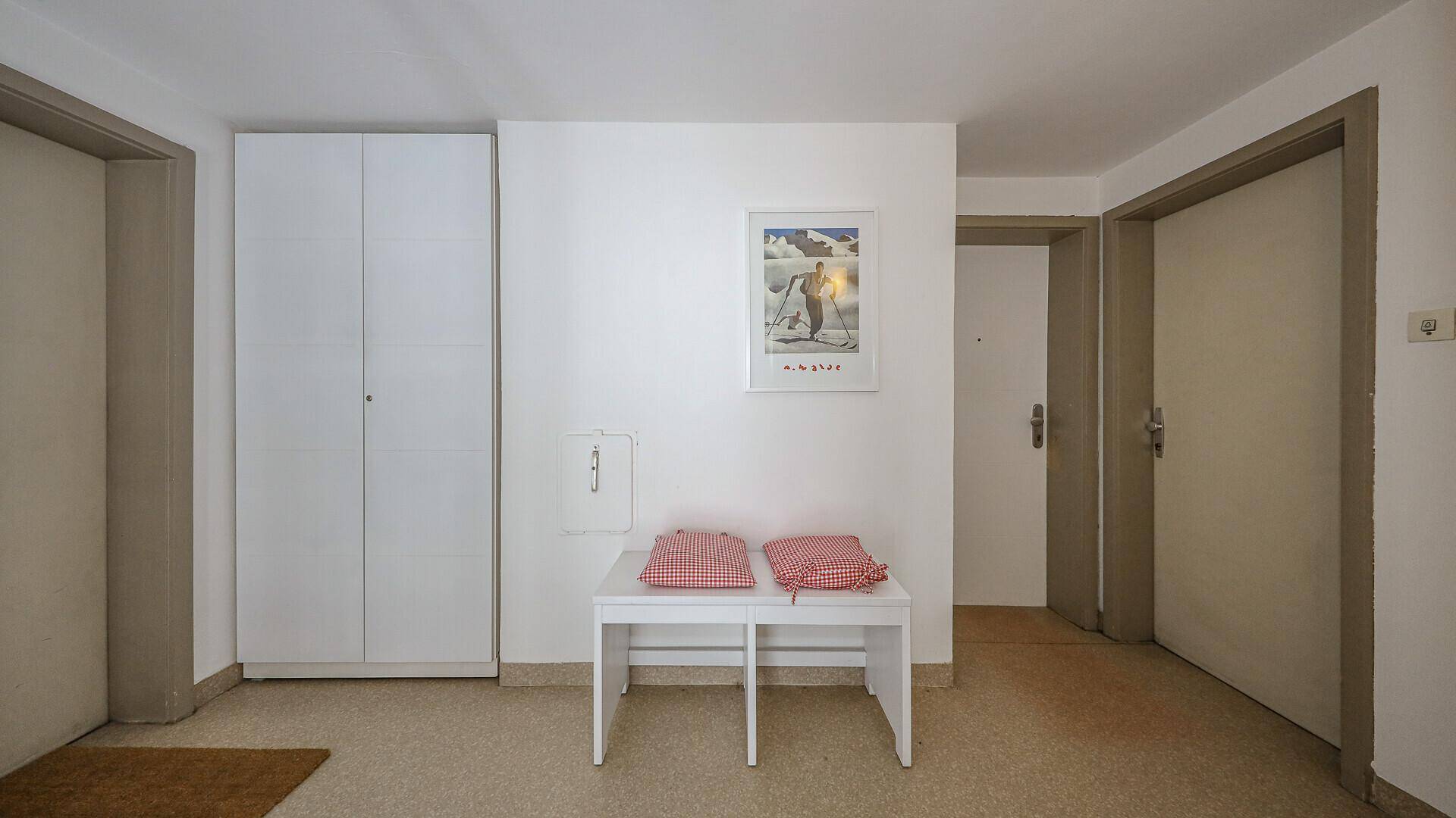 Einfacher Flur mit weißem Schrank und Sitzbank, bietet Zugang zu weiteren Räumen.