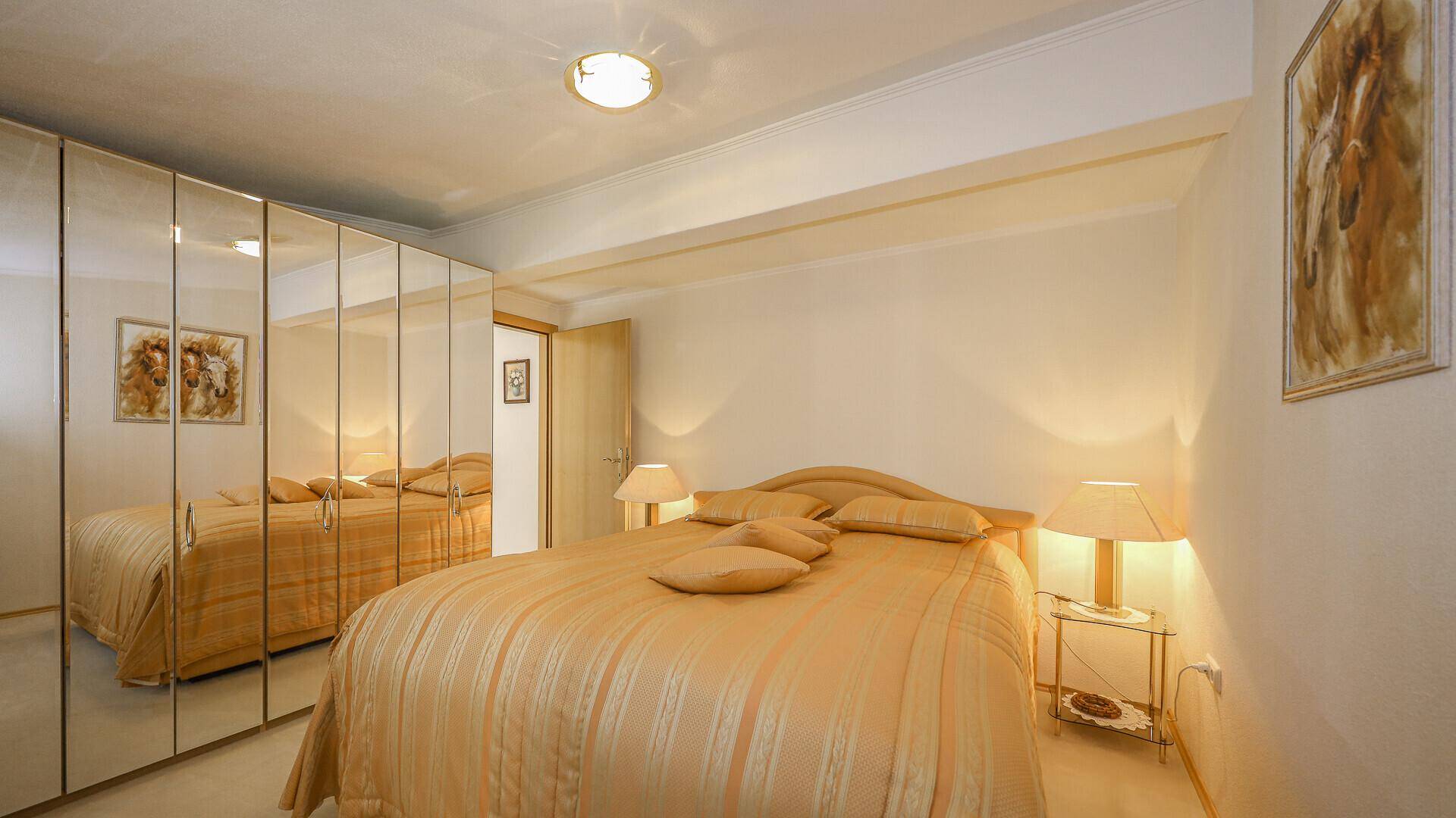 Gemütliches Schlafzimmer mit Doppelbett, Spiegelschränken und warmer Beleuchtung.