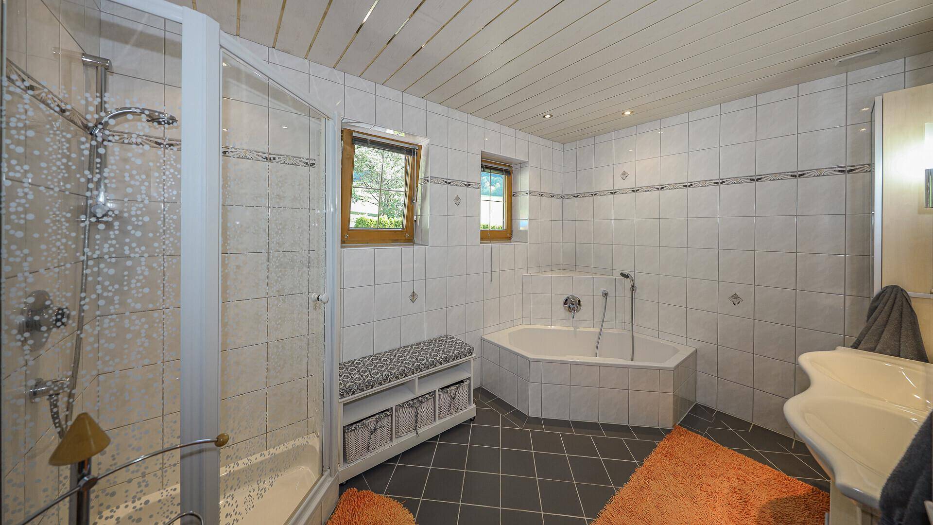 Helles Badezimmer mit Dusche, Eckbadewanne und zwei Fenstern für Tageslicht.
