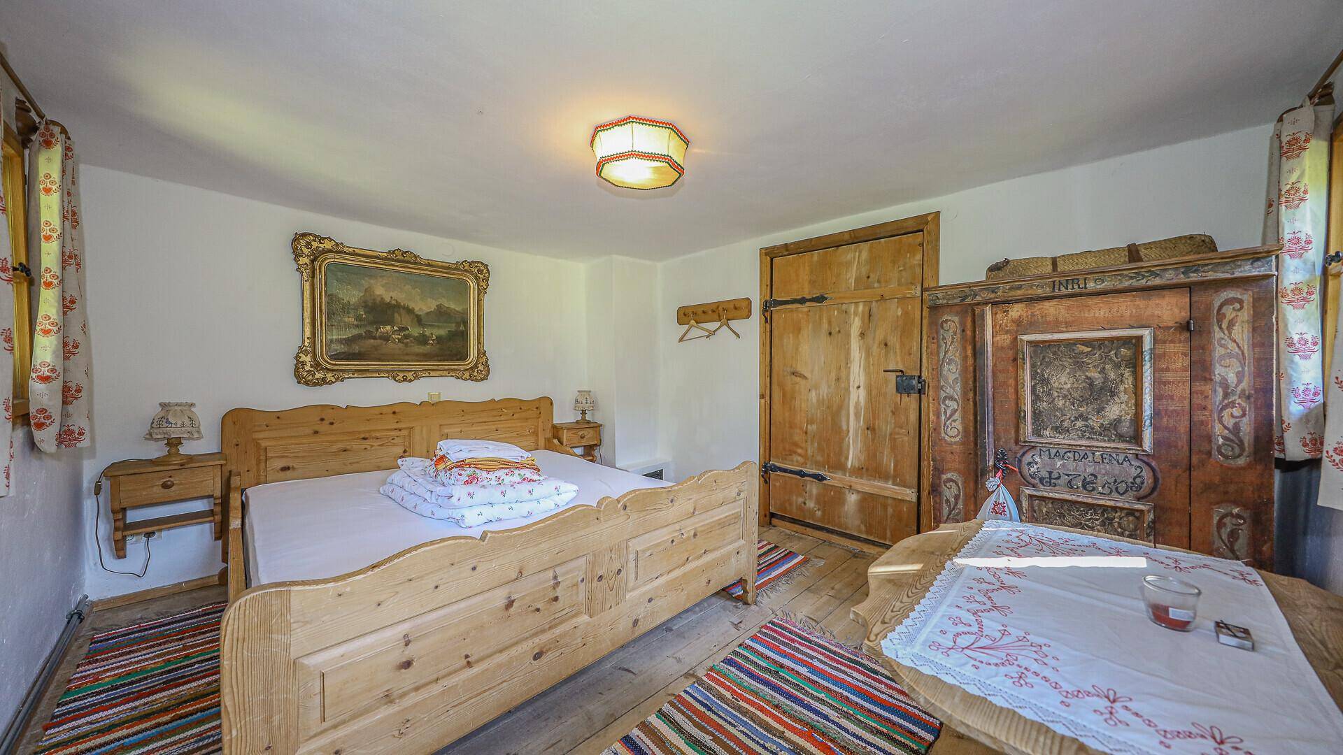 Traditionelles Schlafzimmer mit rustikalen Holzmöbeln, Holzboden und einem farbenfrohen Teppich.