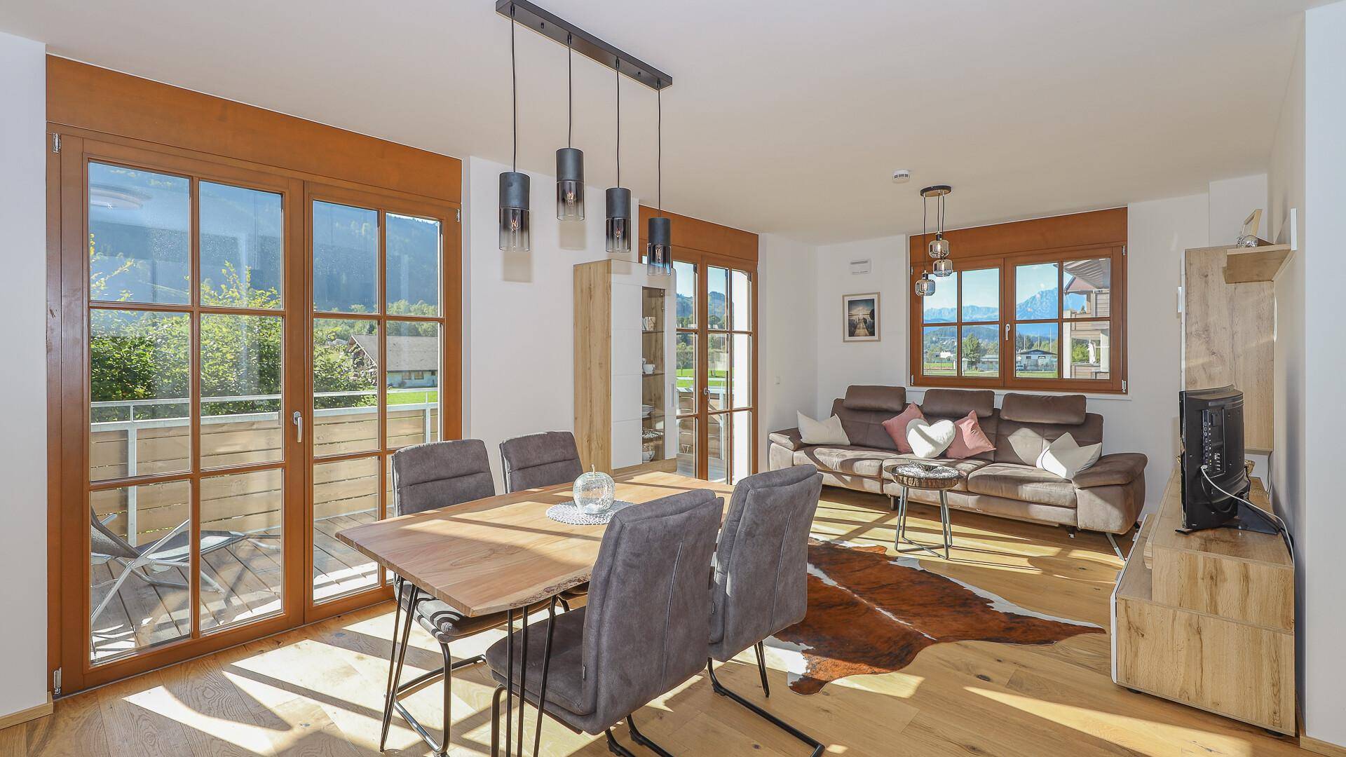 Geräumiger Wohn-Essbereich mit Holzboden, bequemer Couch und Blick auf die Berge.