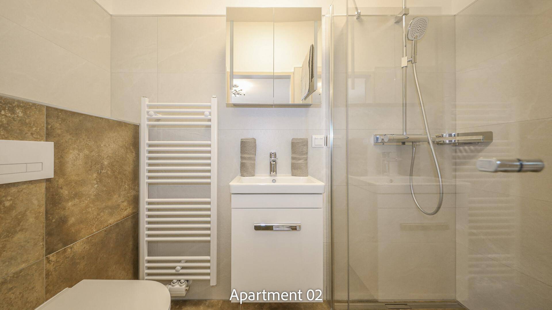 Modernes Badezimmer von Apartment 02 mit eleganten Fliesen, Waschtisch, WC und einer geräumigen Duschkabine.