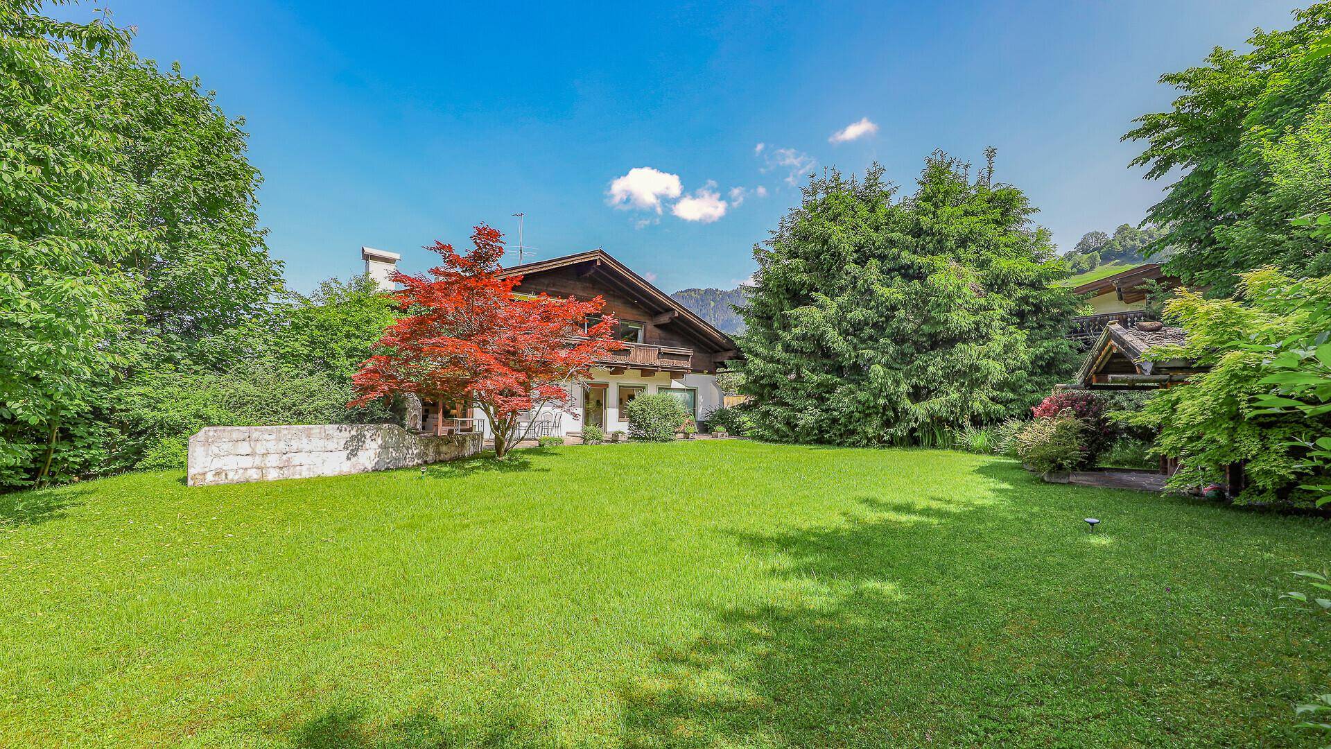 Weitläufige Rasenfläche des Gartens mit altem Baumbestand und einem kleinen Gartenhaus im Hintergrund.