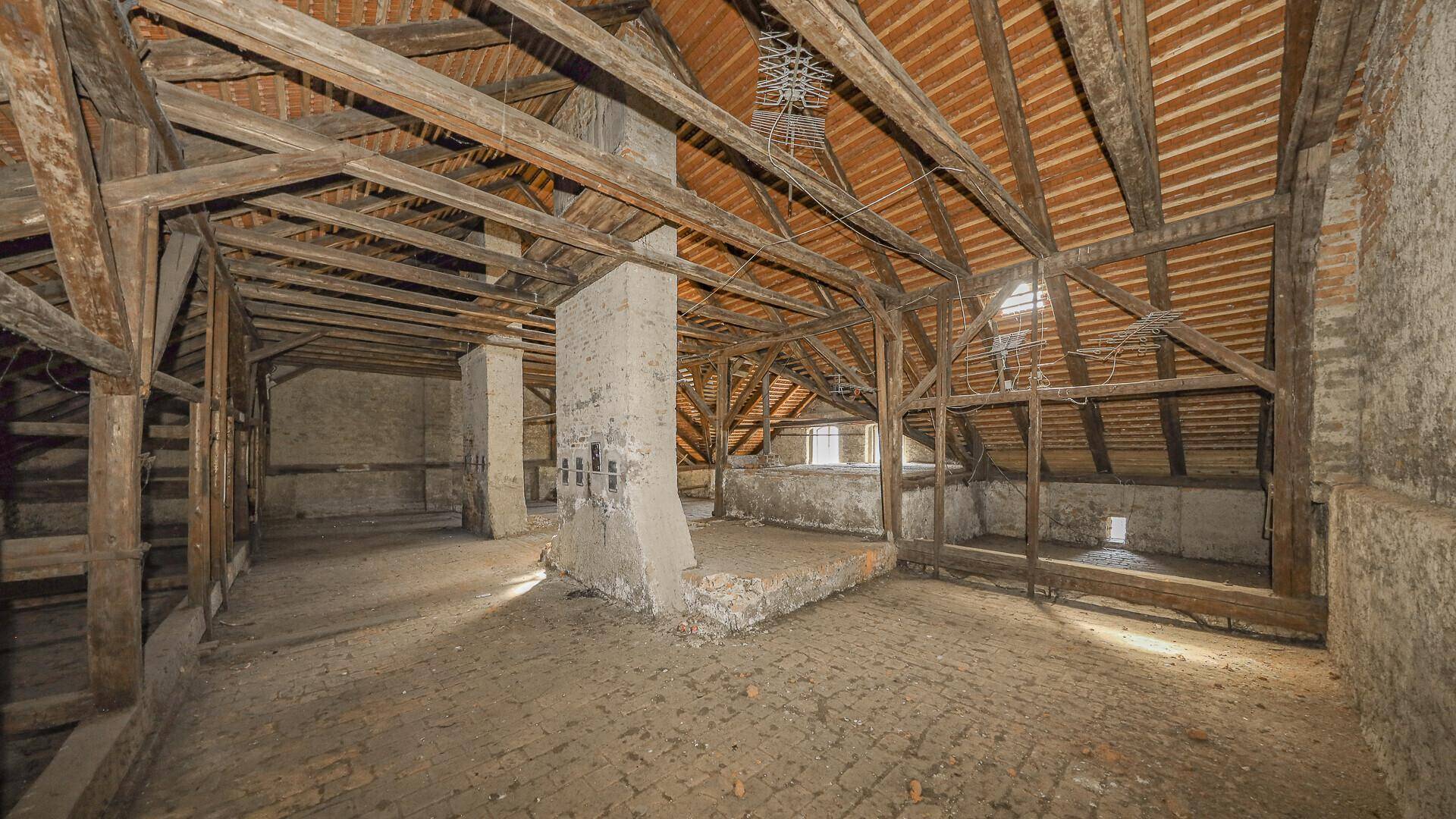 Großer, ungenutzter Dachbodenbereich mit rustikalen Holzbalken und Ziegelboden.