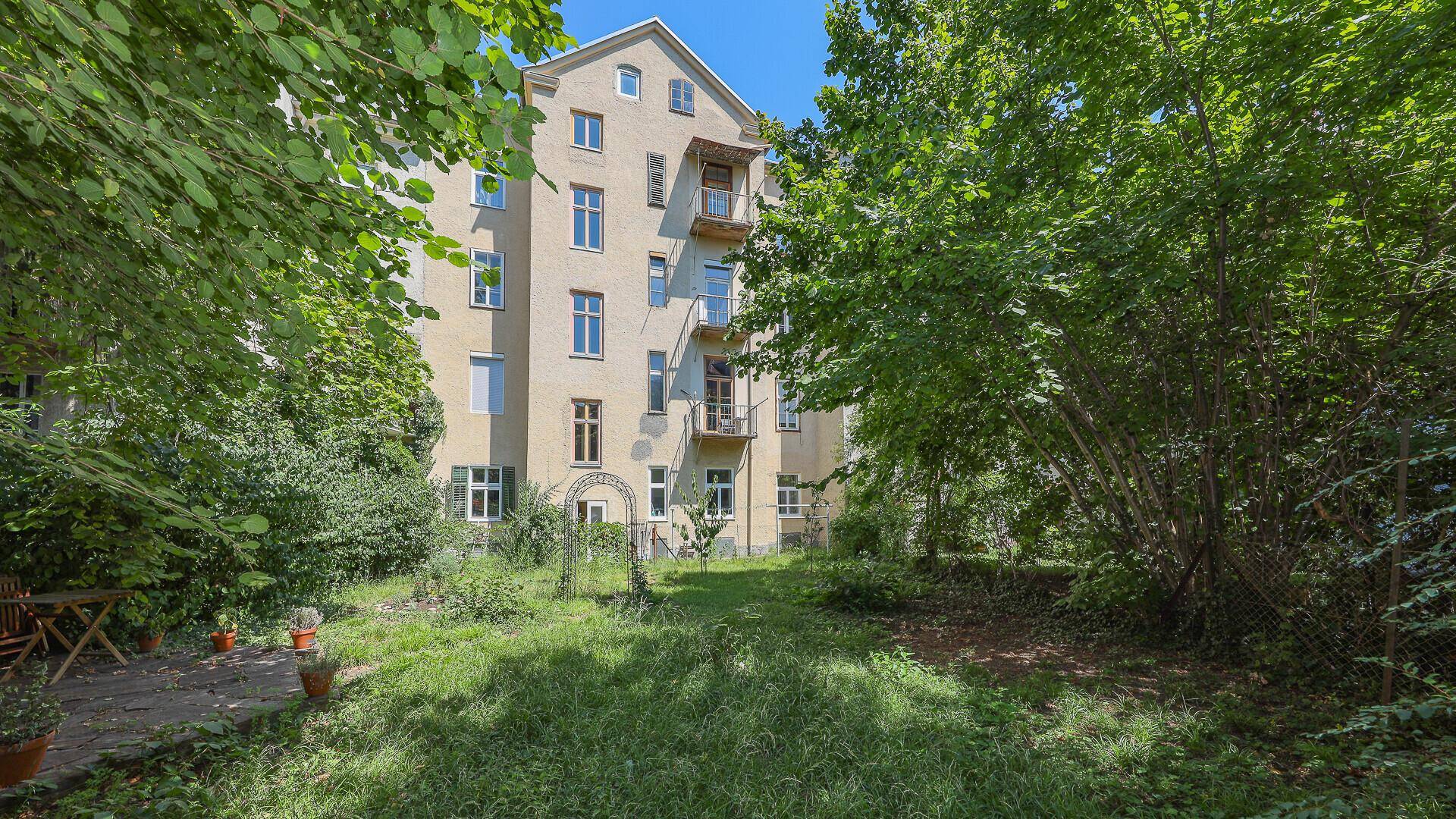 Hinterhofgarten mit altem Baumbestand und Blick auf die Gebäudefassade.