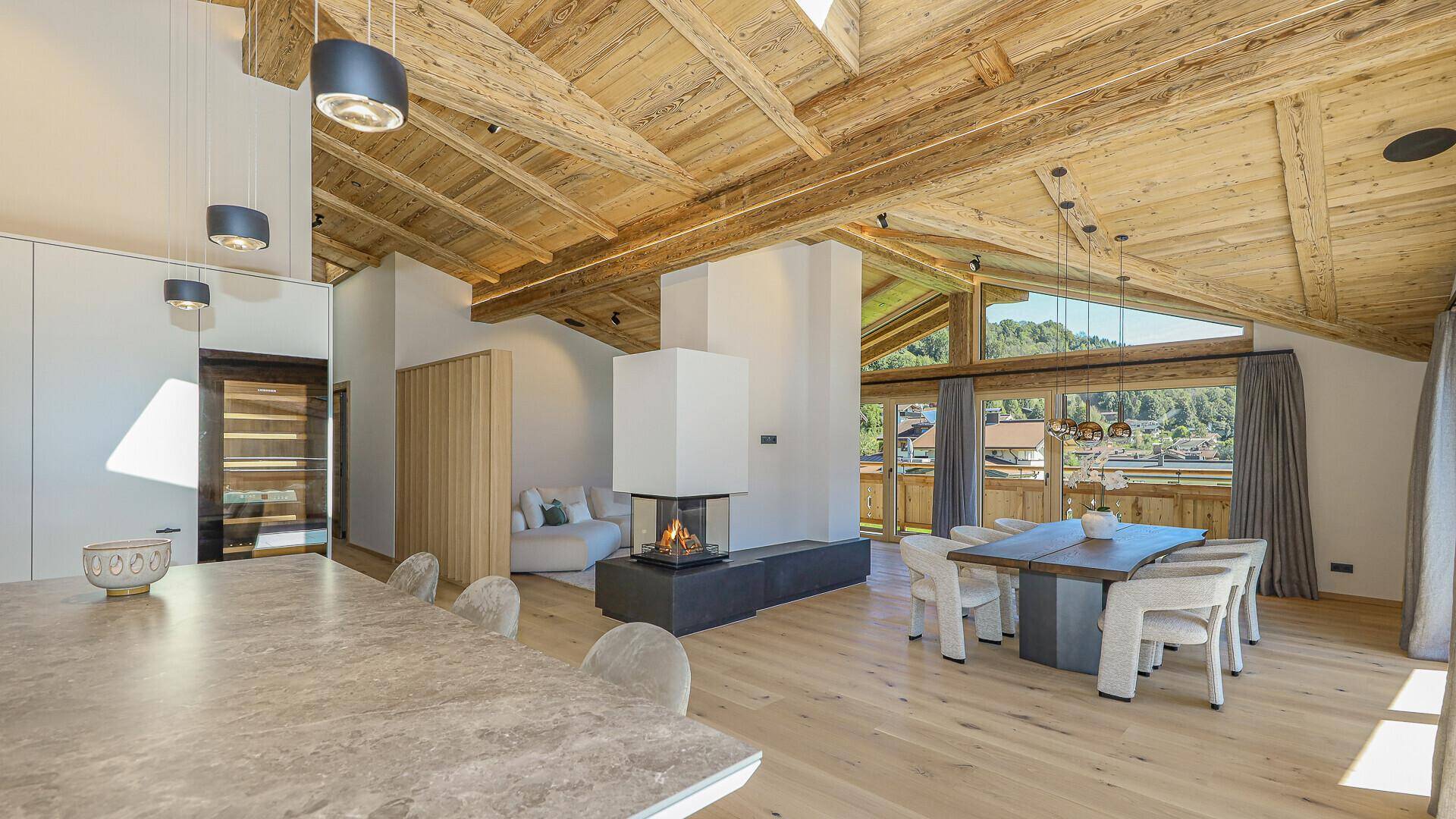 Heller Wohn- und Essbereich mit Kamin, Holzbalkendecke und Blick auf die Berge.