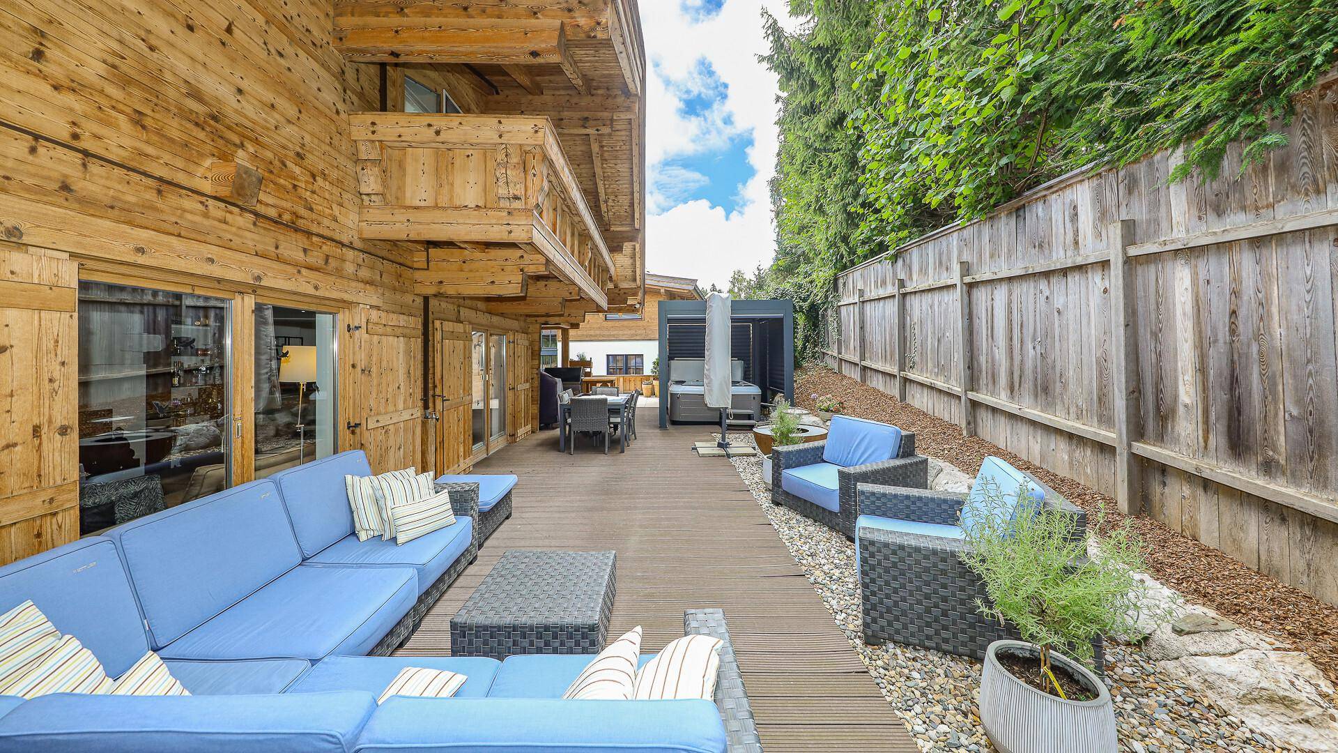 Große Holzterrasse mit bequemen Loungemöbeln und umzäuntem Gartenbereich.
