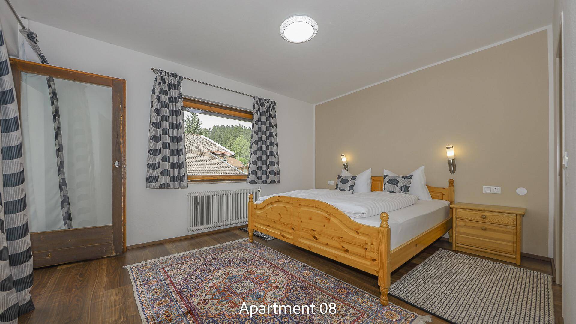 Schlafzimmer von Apartment 08 mit rustikalem Holzdoppelbett, Nachttischen und einem gemusterten Teppich auf Holzboden.