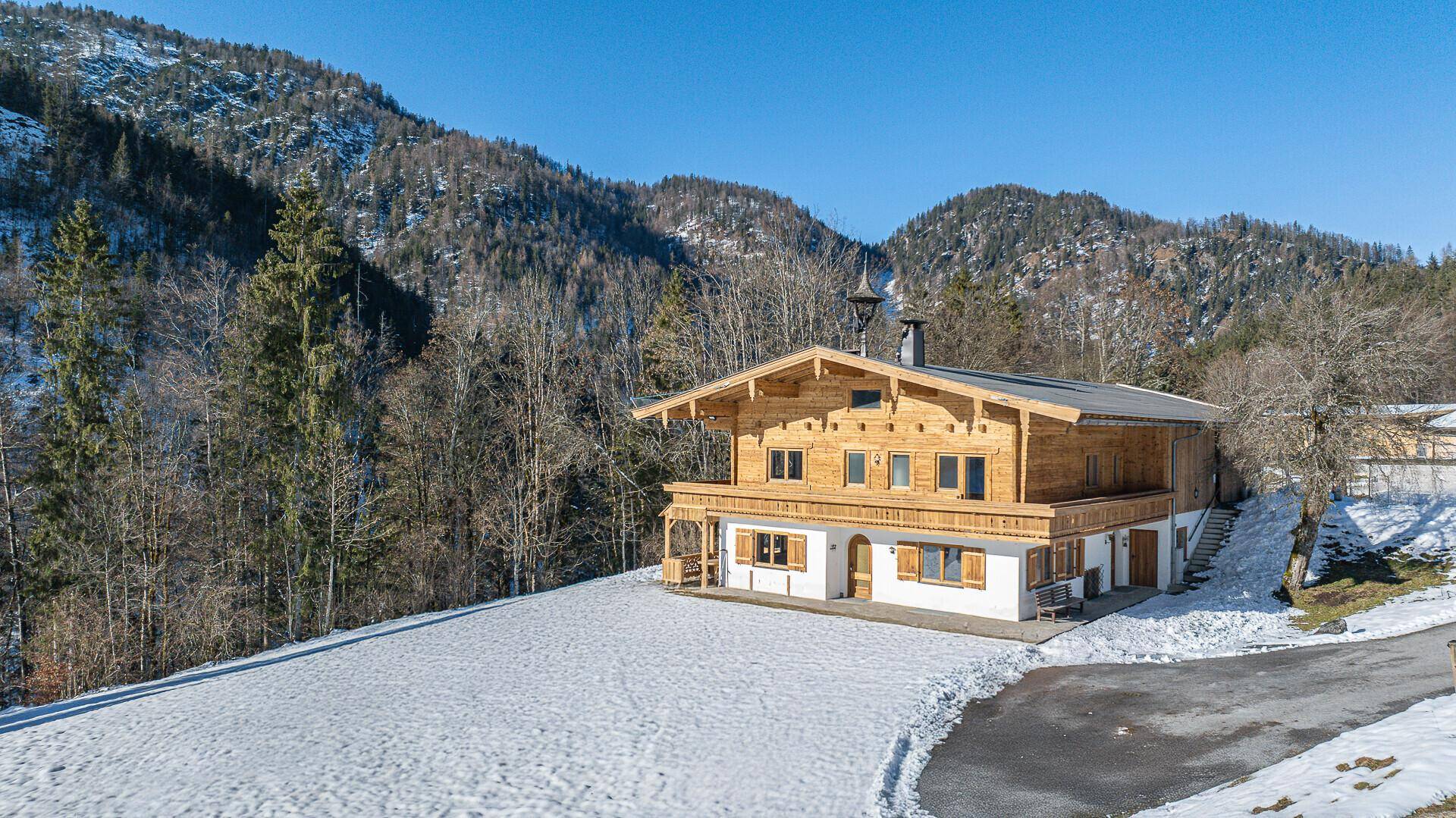 Alpines Chalet mit Holzbalkonen und schneebedeckten Hängen im Hintergrund.