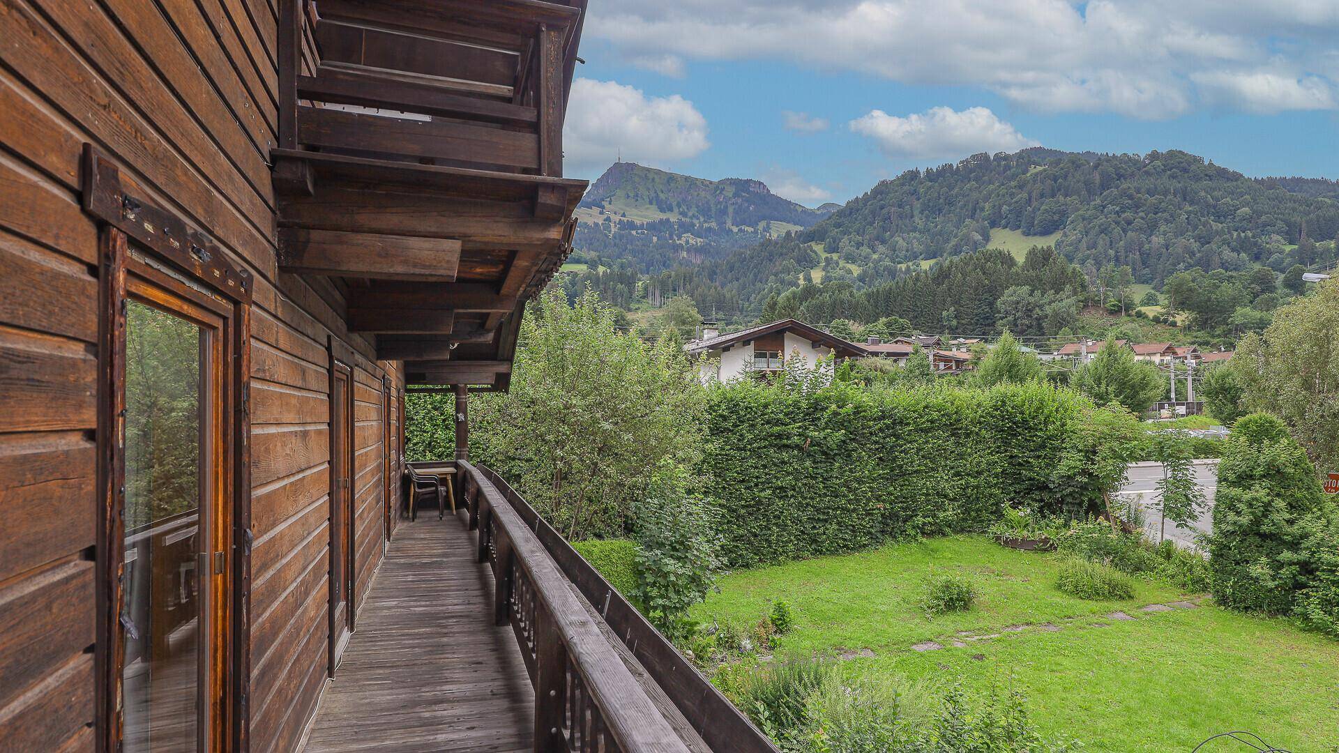 Langer Holzbalkon mit weitem Blick über grüne Hügel und die umliegende Bebauung.
