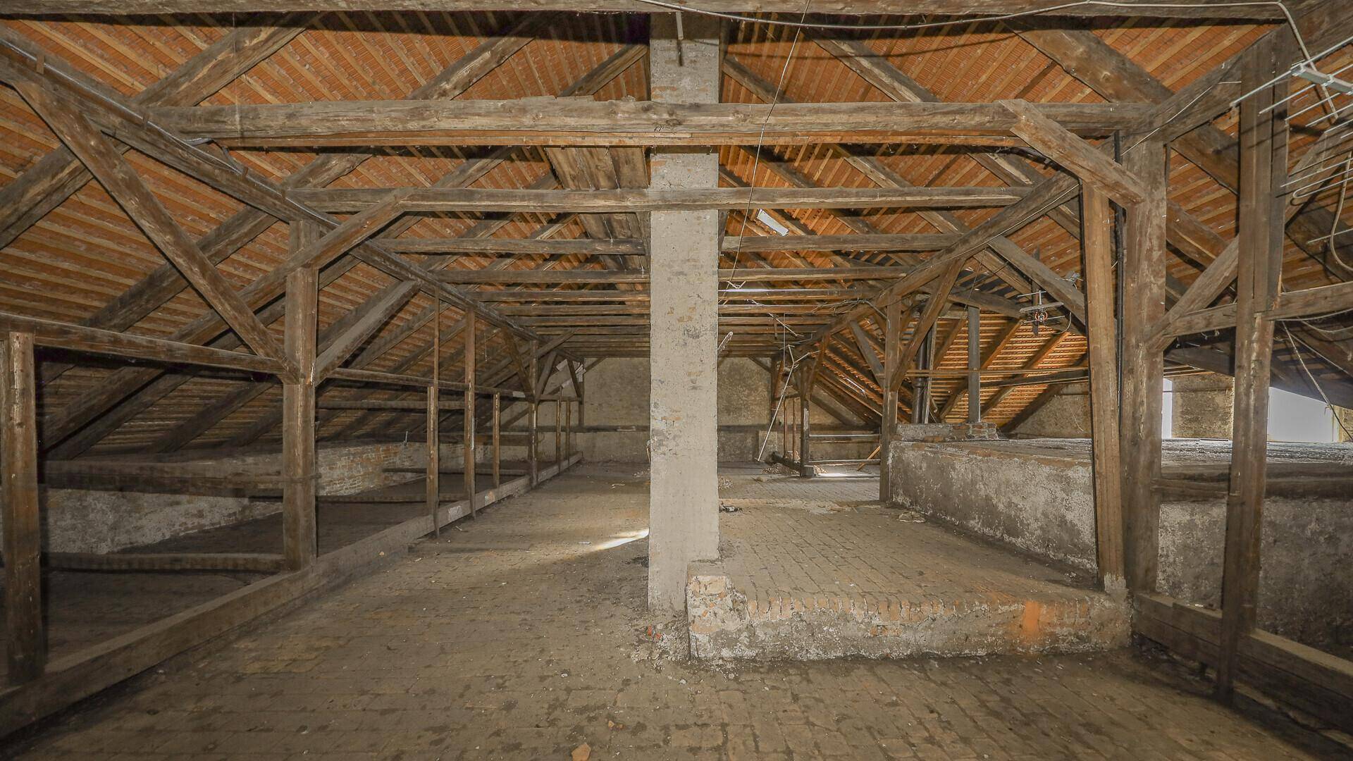 Weitläufiger Dachboden mit sichtbarer Holzkonstruktion und Ziegelboden, ideal für zukünftige Nutzung.