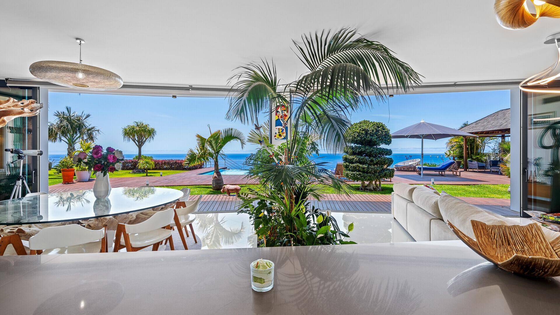 Heller Wohn- und Essbereich mit großen Glasfronten, die einen direkten Zugang zum Garten und Meerblick bieten.