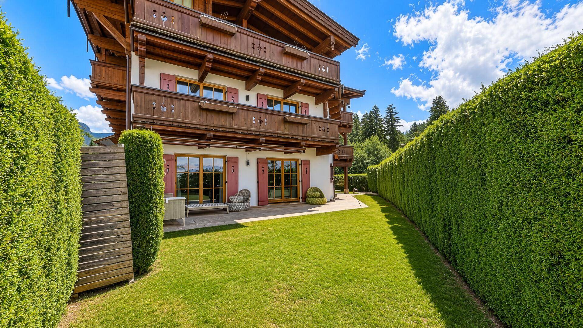 Gepflegter Gartenbereich mit Rasenfläche und hoher Hecke vor einem traditionellen Gebäude.
