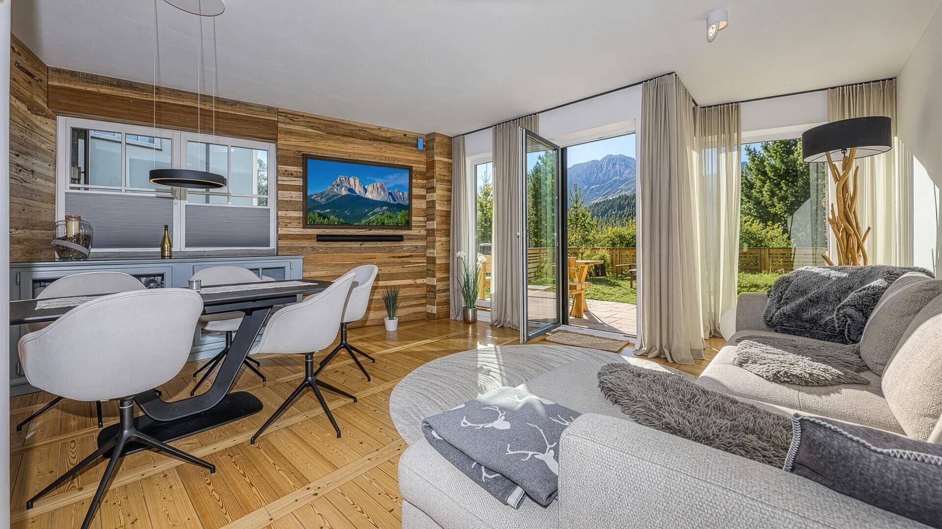 Heller Wohn- und Essbereich mit Holzakzenten, modernem Mobiliar und direktem Zugang zum Garten mit Bergblick.