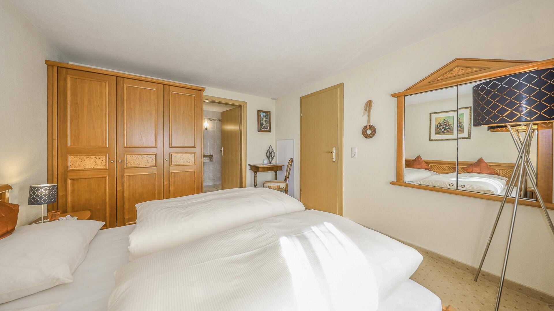 Gemütliches Schlafzimmer mit Doppelbett, Holzschrank und Spiegel, hell beleuchtet.