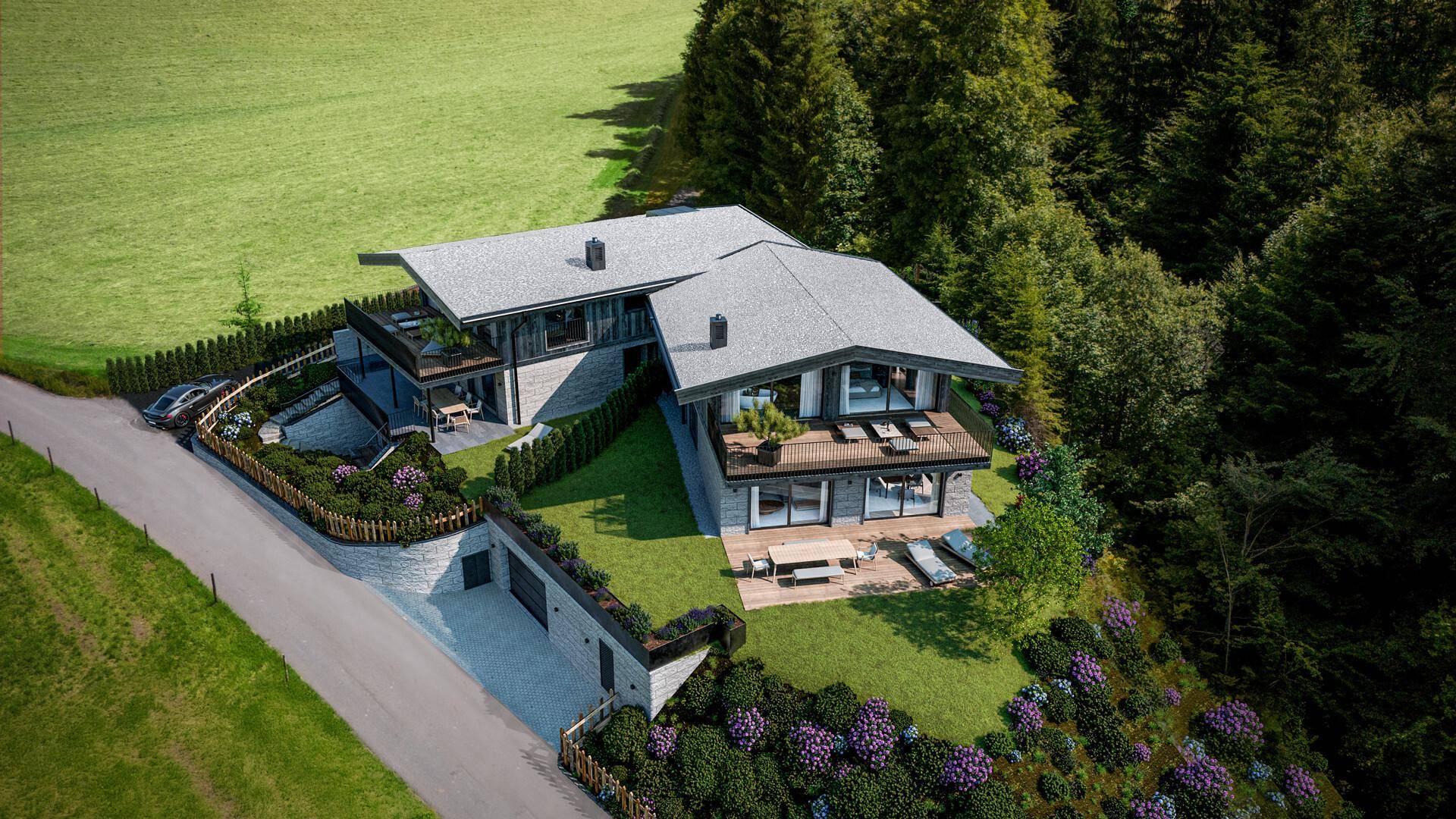 Luftaufnahme eines modernen Hauses mit weitläufigem Garten und angrenzenden Wäldern in den Bergen.
