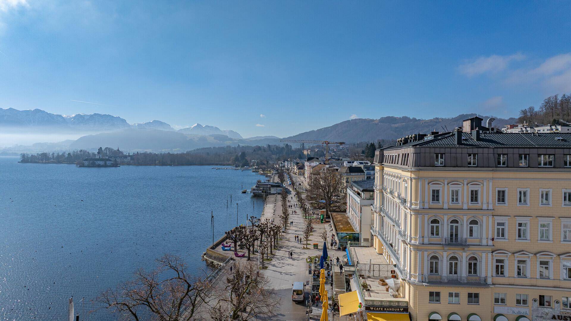 Luftaufnahme der Uferpromenade und des Sees, umgeben von einer beeindruckenden Bergkulisse.