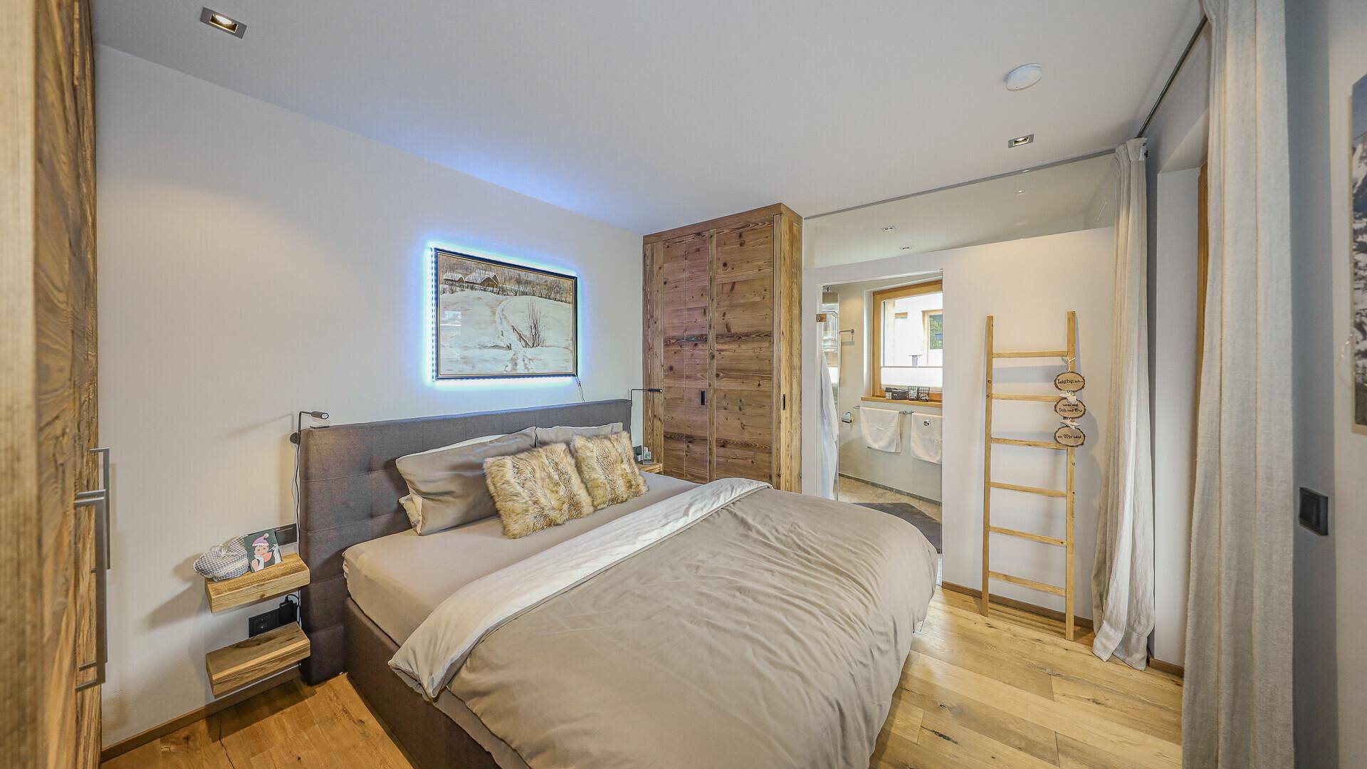 Modernes Schlafzimmer mit Doppelbett, Holzelementen und indirekter Beleuchtung.